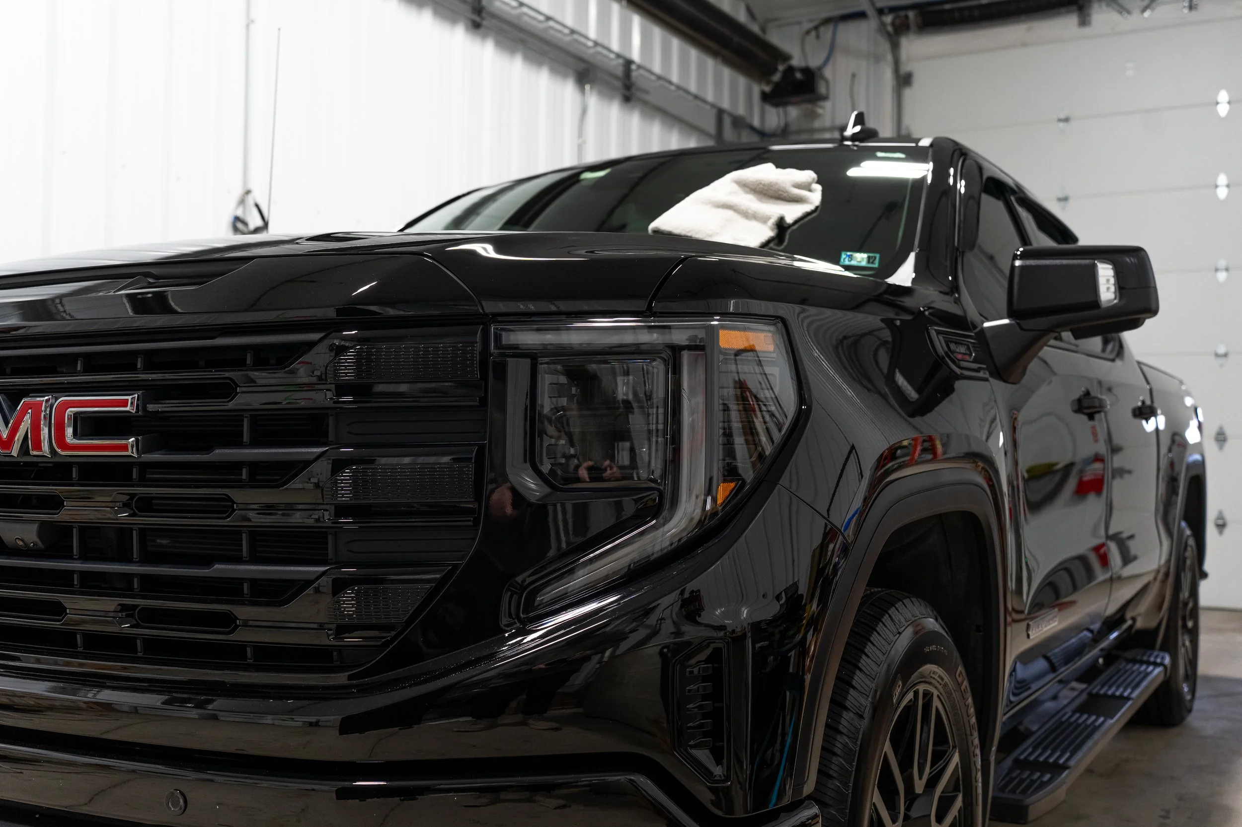 Black GMC pickup truck inside a garage, with a white towel on the windshield and various garage doors in the background.
