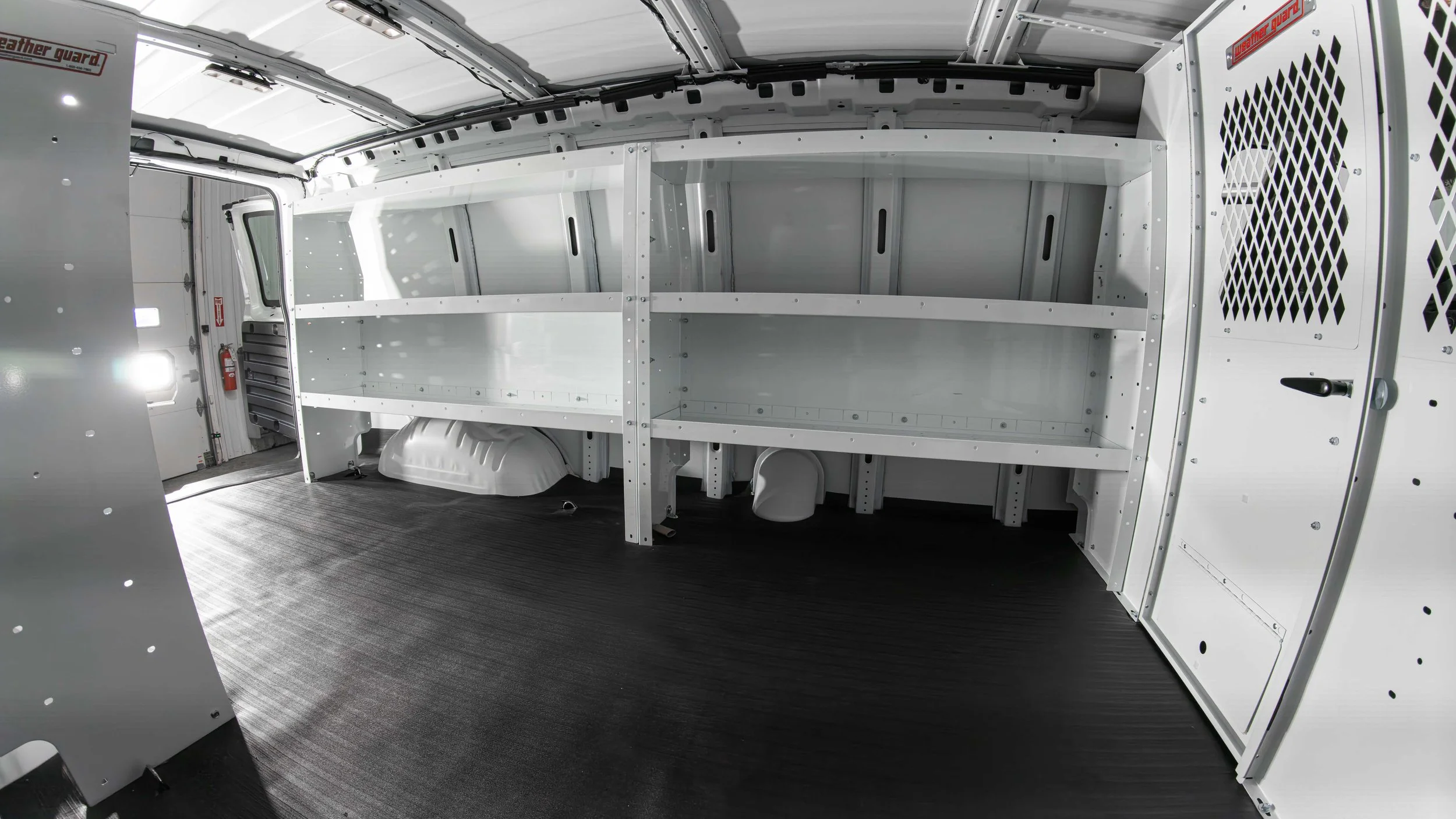 Driver-side WeatherGuard shelving, screened partition, and rubber cargo flooring inside a Chevy Express work van