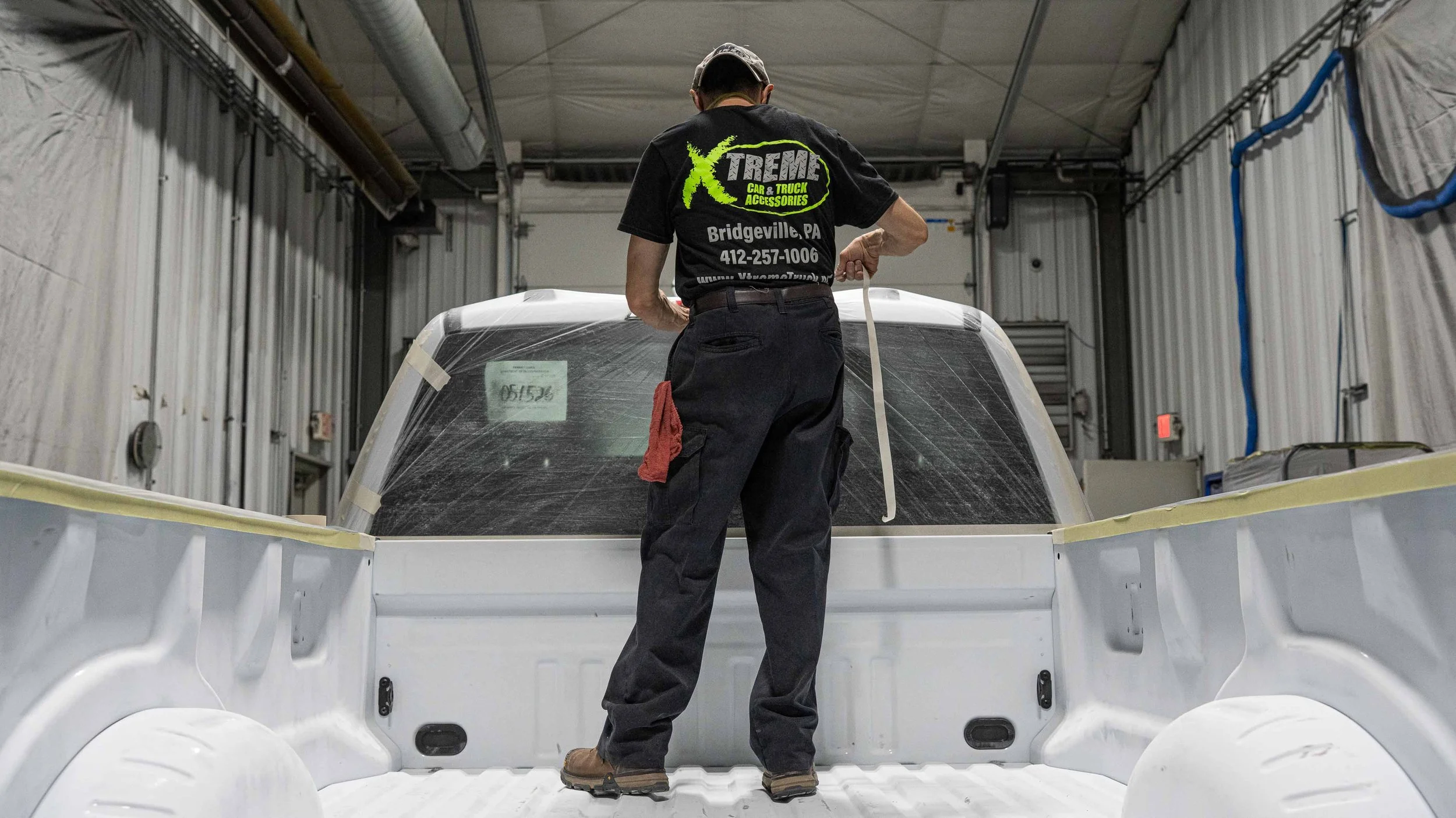 Xtreme Car & Truck Accessories technician preparing a white pickup truck bed for professional spray-in bed liner installation in Bridgeville, PA, showing the masking and prep process before coating.
