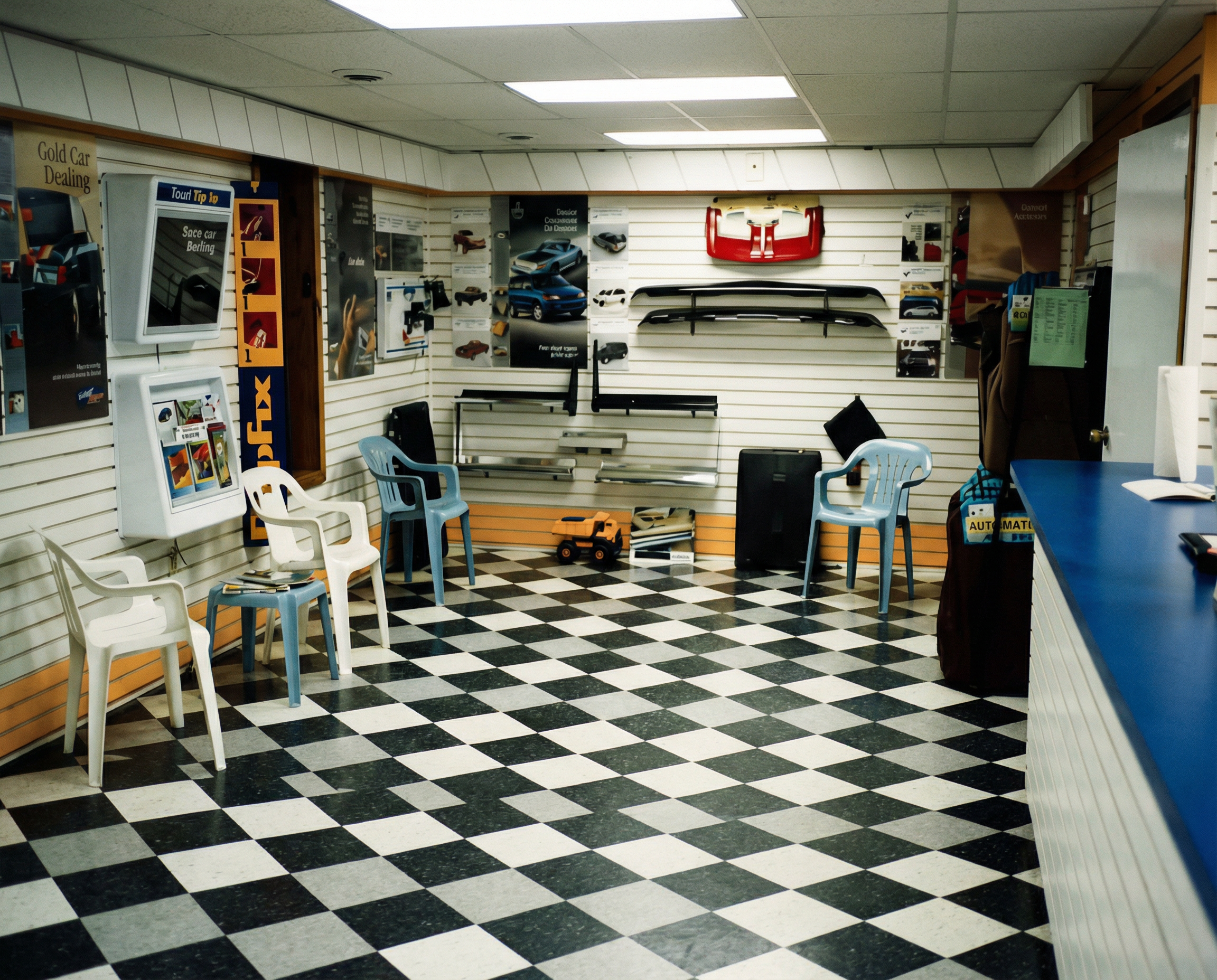 Inside an auto parts shop with black and white checkered floor, blue countertop, and walls with car accessories, posters, and racks of car parts.