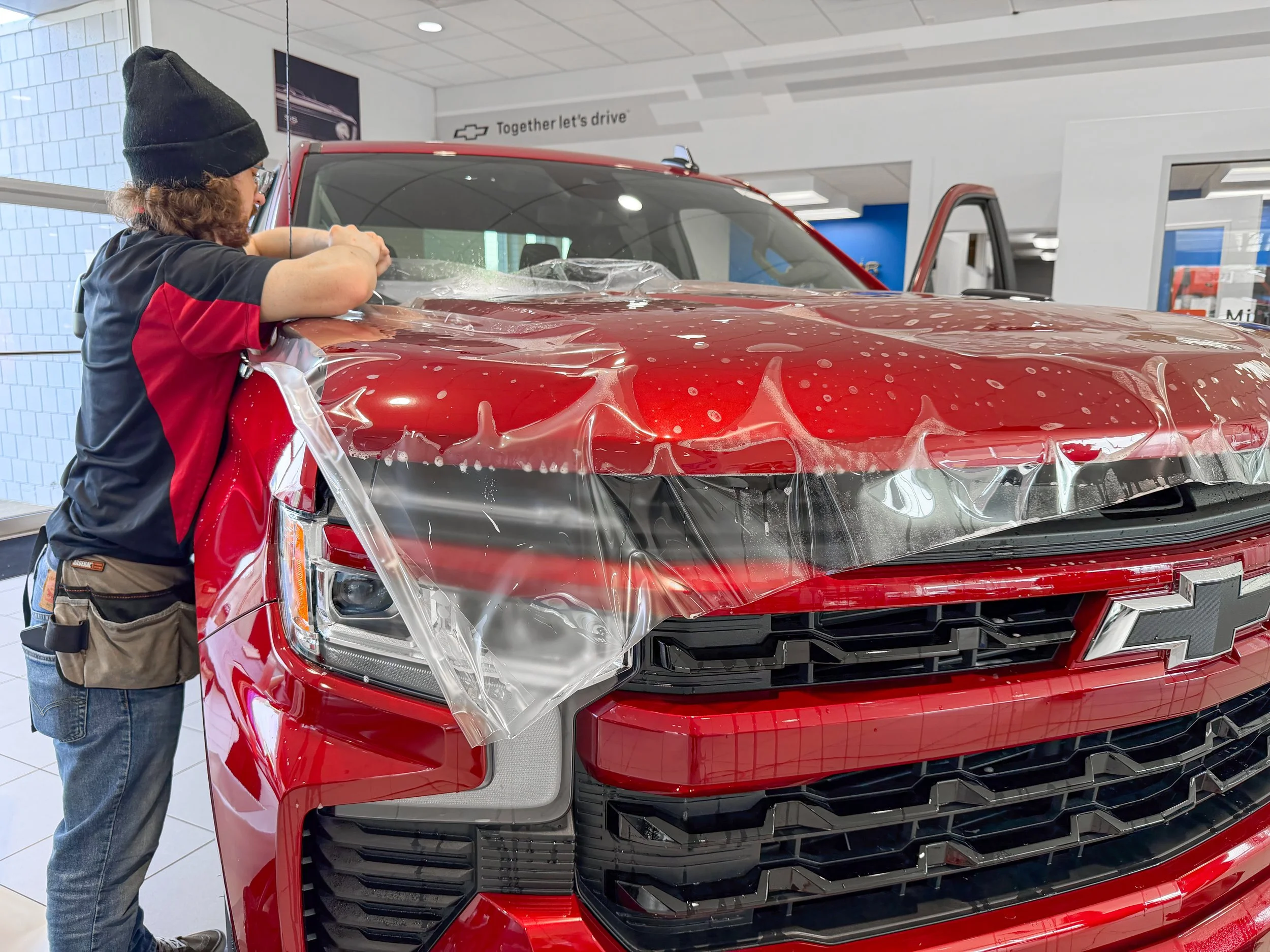 Xtreme installer positioning XPEL paint protection film across the hood and front end of a red Chevy truck in Bridgeville, PA.