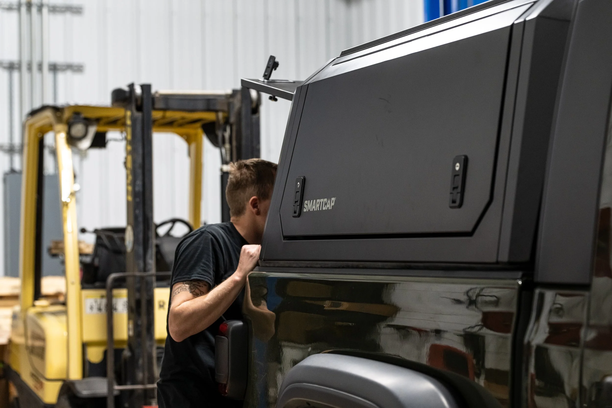 A man peeks into a black vehicle with a SmartCap storage compartment. A yellow forklift is in the background inside a warehouse.