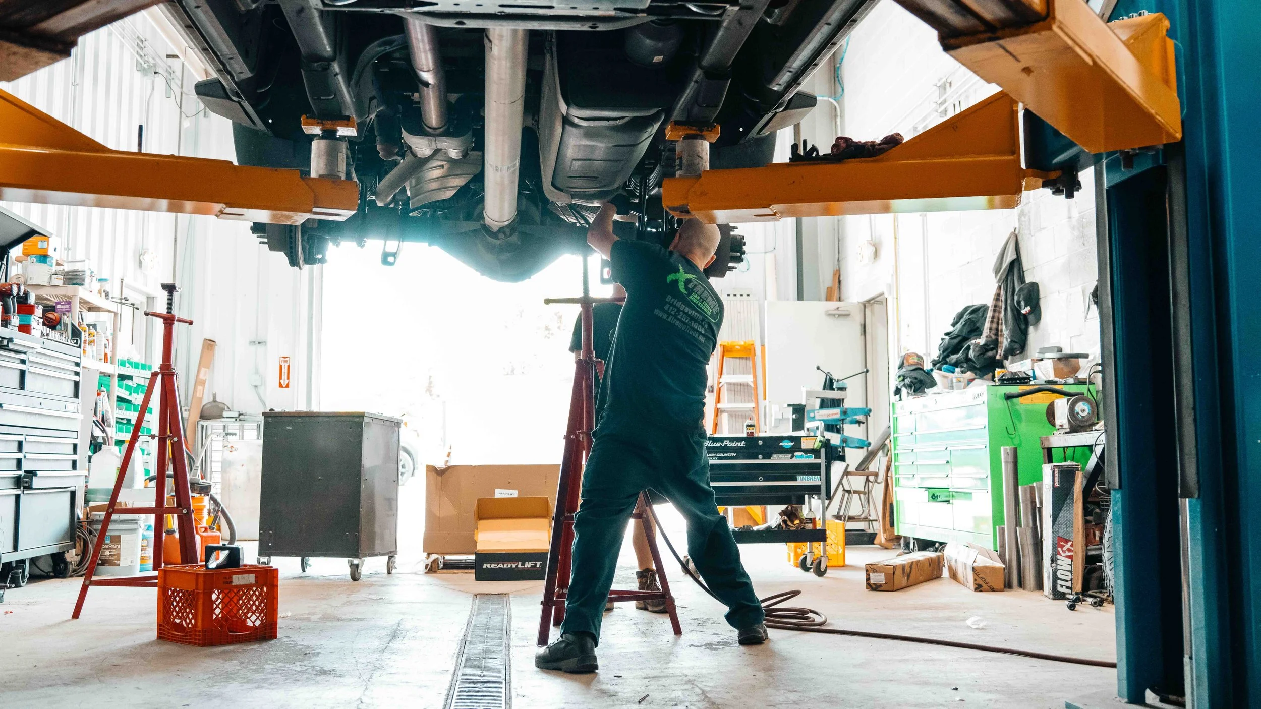 GMC Sierra on a lift while a technician works underneath during ReadyLIFT suspension lift installation.