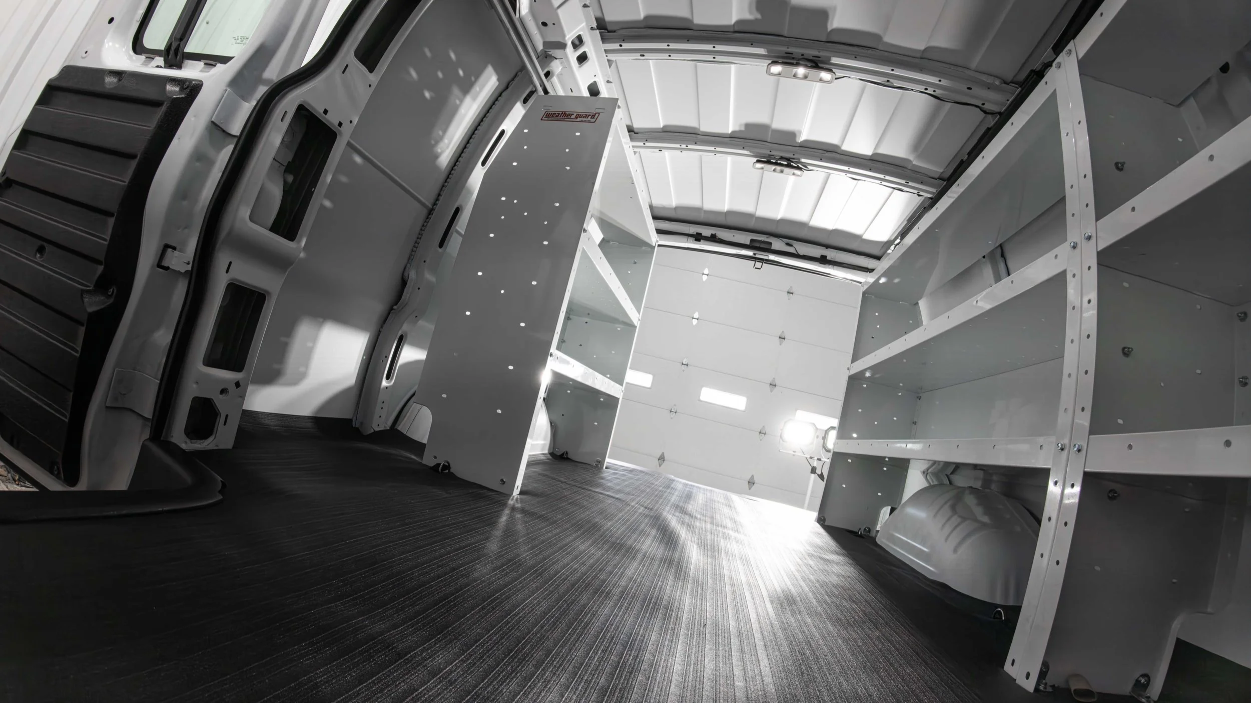 Floor-level view of a Chevy Express cargo area with WeatherGuard shelving and black rubber van flooring