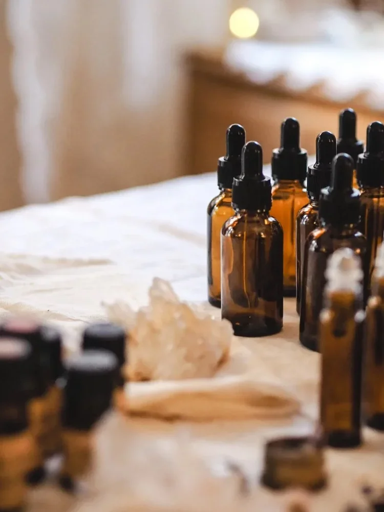 Several amber glass dropper bottles arranged on a table with a cream-colored cloth, with a large dried flower or plant and some blurred objects in the foreground.