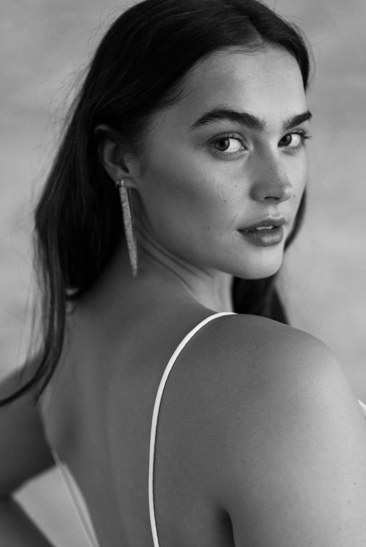 A radiant bride wearing natural ethical bridal makeup, glowing skin with a soft dewy finish, subtle champagne shimmer on the eyelids, softly defined brows, delicate rose-toned blush, and a muted petal-pink lip. Her complexion looks fresh breathable.
