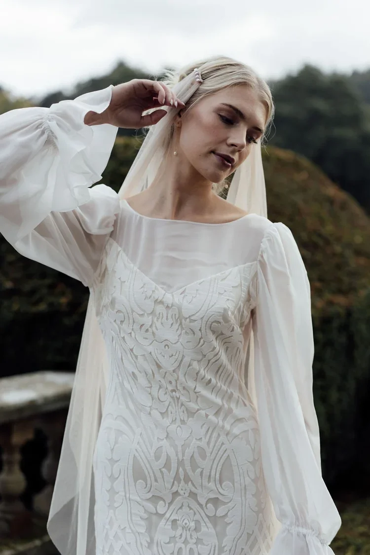 A radiant bride wearing natural ethical bridal makeup, glowing skin with a soft dewy finish, subtle champagne shimmer on the eyelids, softly defined brows, delicate rose-toned blush, and a muted petal-pink lip. Her complexion looks fresh breathable.
