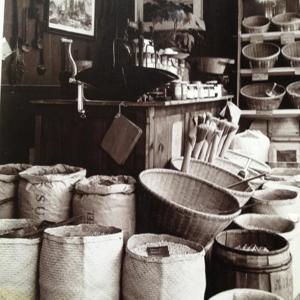 Inside a rustic store with baskets, bags, and wooden shelves displaying kitchen and gardening items.