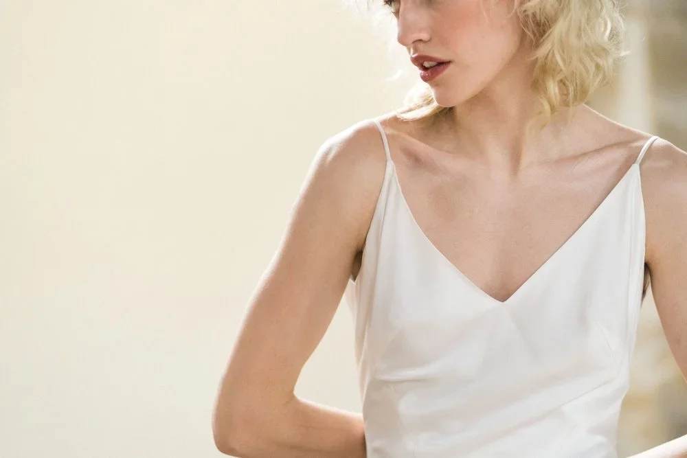 Close-up of a woman with blonde hair wearing a white spaghetti strap dress.