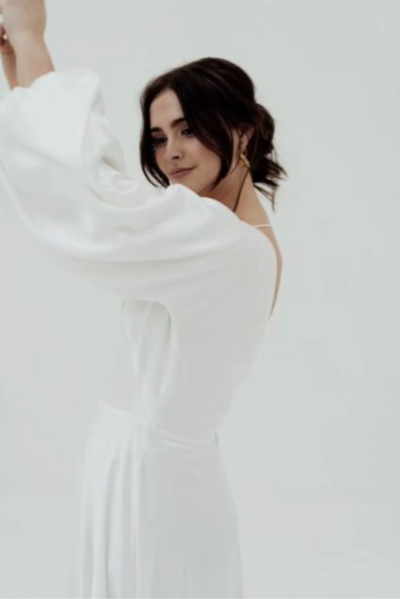 A woman with short dark hair in a white dress against a plain white background.