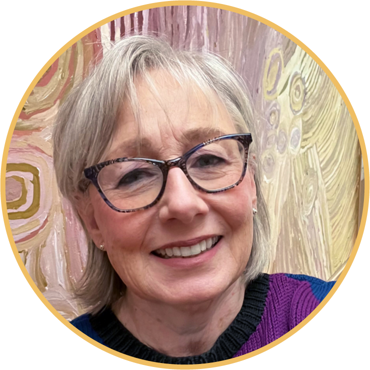 A smiling elderly woman with gray hair and glasses, wearing a purple and black top, standing in front of an abstract art background.