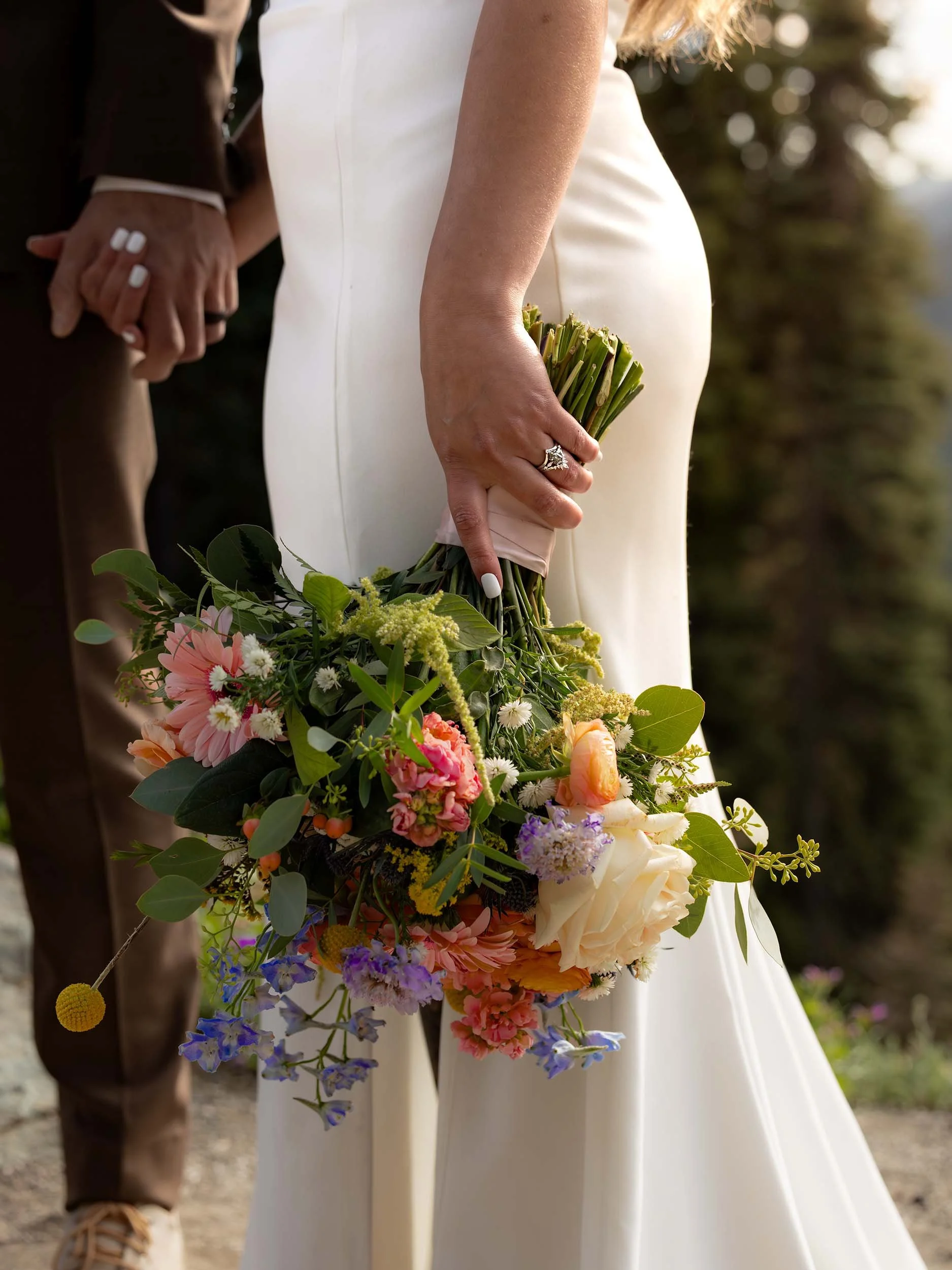 Cropped in focus on a bride's colorful bouquet and wedding rings as she holds her husband's hand at their Tipsoo Lake elopement.