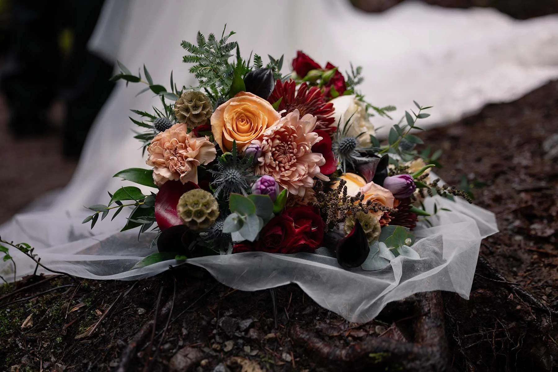 A bold, colorful wedding bouquet lays on a long bridal veil sitting on the ground at an elopement in Olympic National Park.