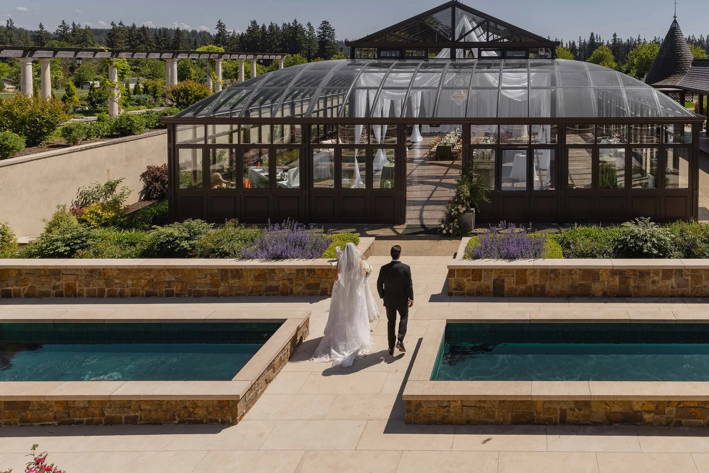 A bride and groom walk through the elaborate courtyard of their wedding venue toward the atrium for their reception. Chateau De Lis is a European inspired luxury venue in Oregon.