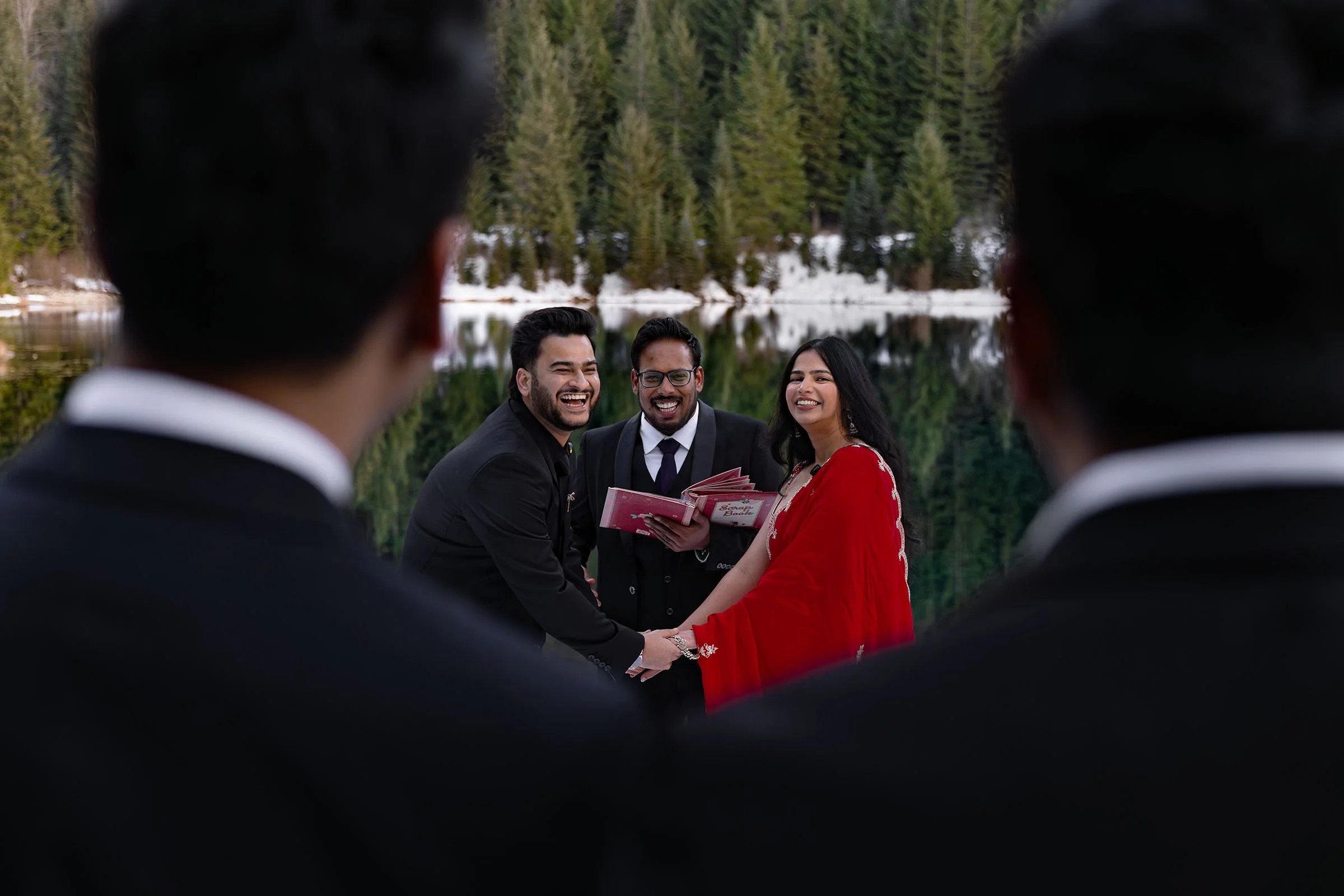 An Indian couple and their officiant laugh during their winter intimate wedding ceremony at Gold Creek Pond.