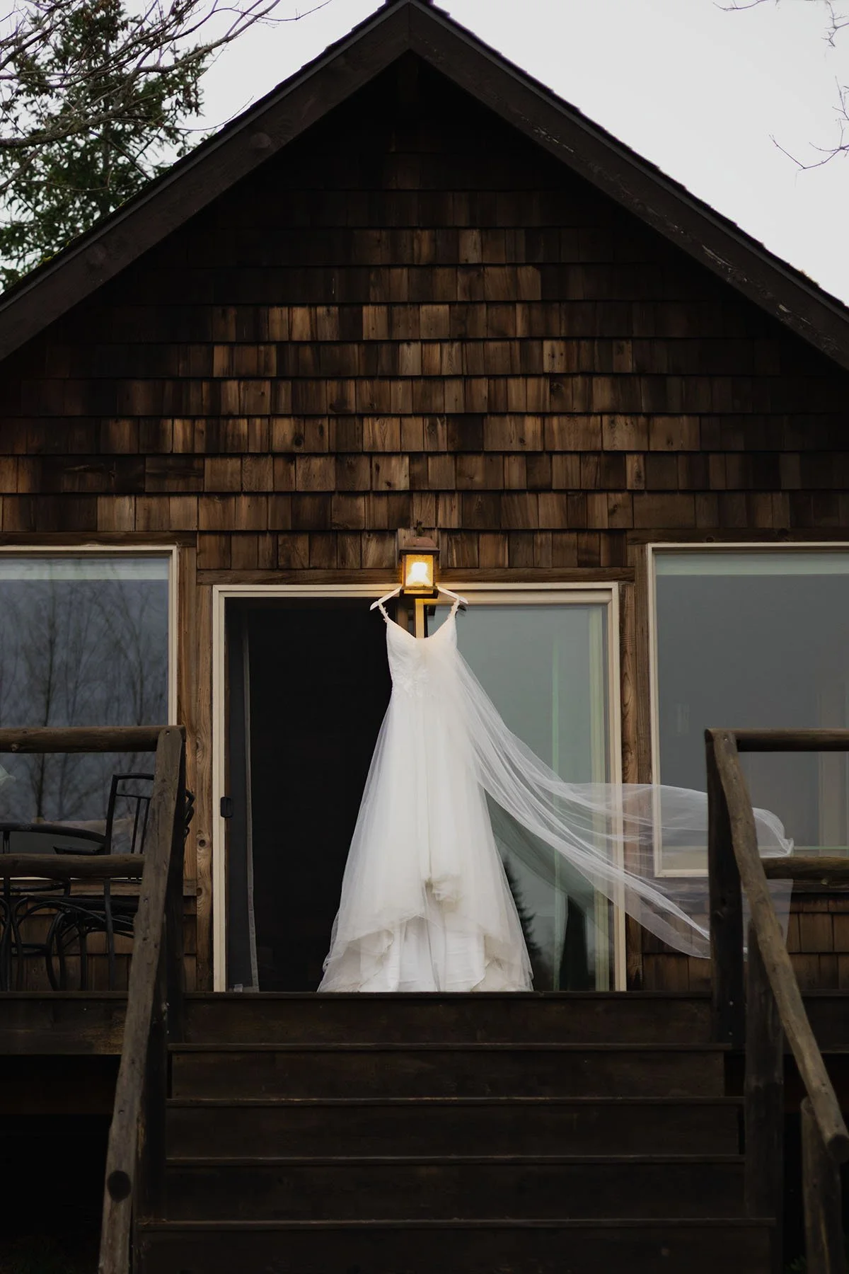 A wedding dress hangs on a cabin porch light and the veil blows in the breeze in Port Angeles