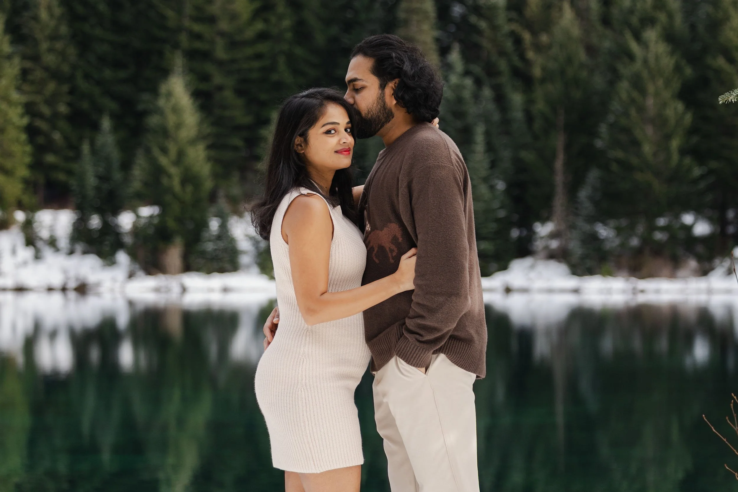An expecting couple embrace at Gold Creek Pond during their winter maternity and gender reveal session.