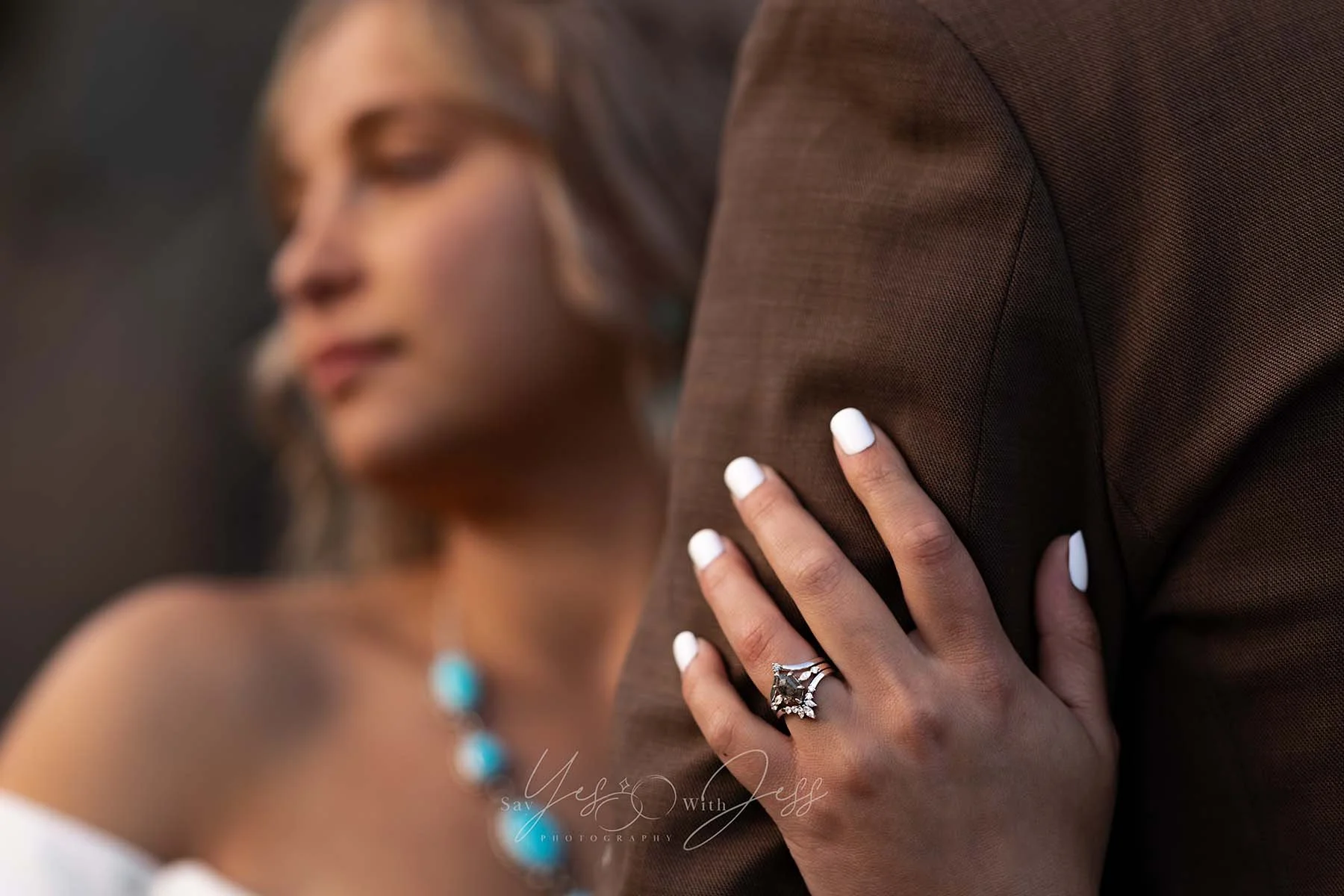 A bride wraps her hand around her husband's arm, showing off her custom wedding ring stack on their wedding day.