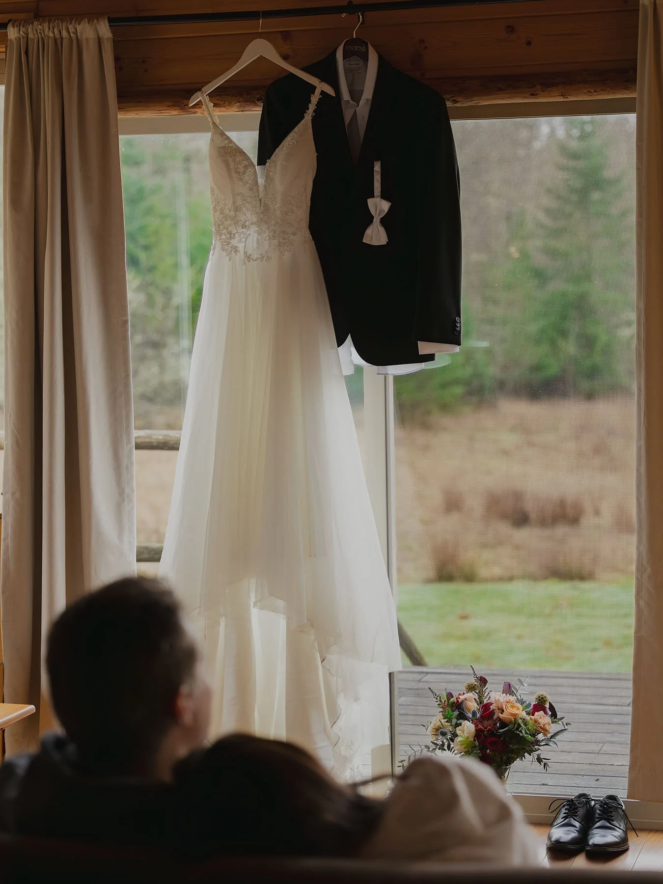 A couple snuggle on the couch looking at their wedding attire hanging in the window of their Port Angeles cabin bnb.