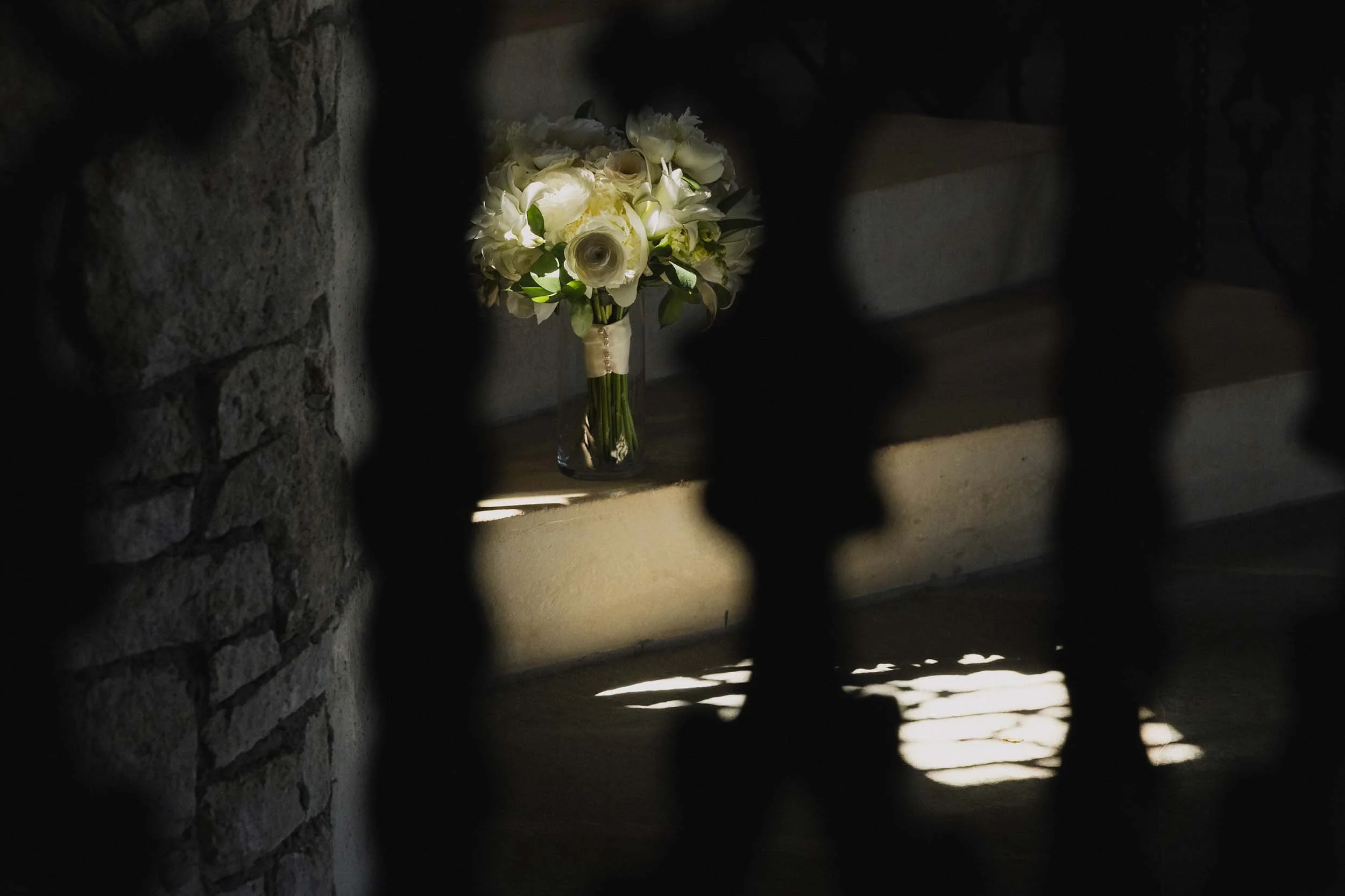 A white and green bridal bouquet rests on the spiral, stone staircase at Chateau De Lis. As photographed through the ornate wrought-iron railing.