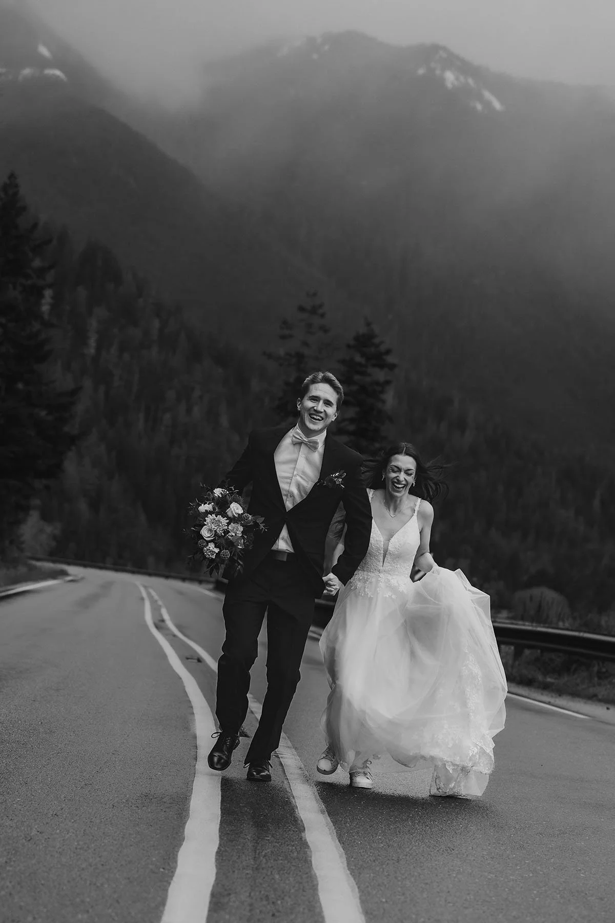 A couple in wedding attire run in the road near the Lake Crescent welcome sign in Olympic National Park