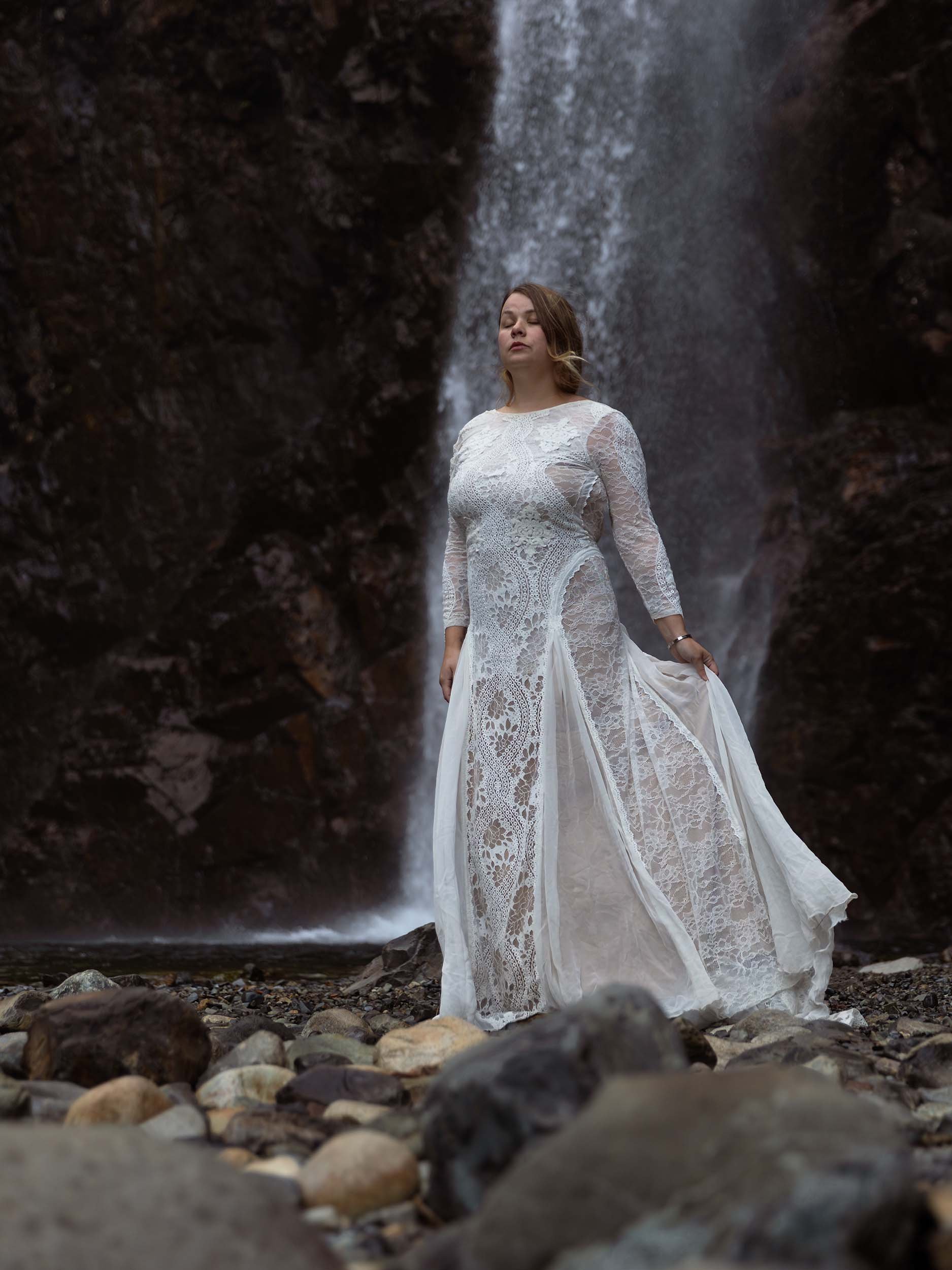 Bride stands in front of Franklin Falls in a moody photograph from an elopement.
