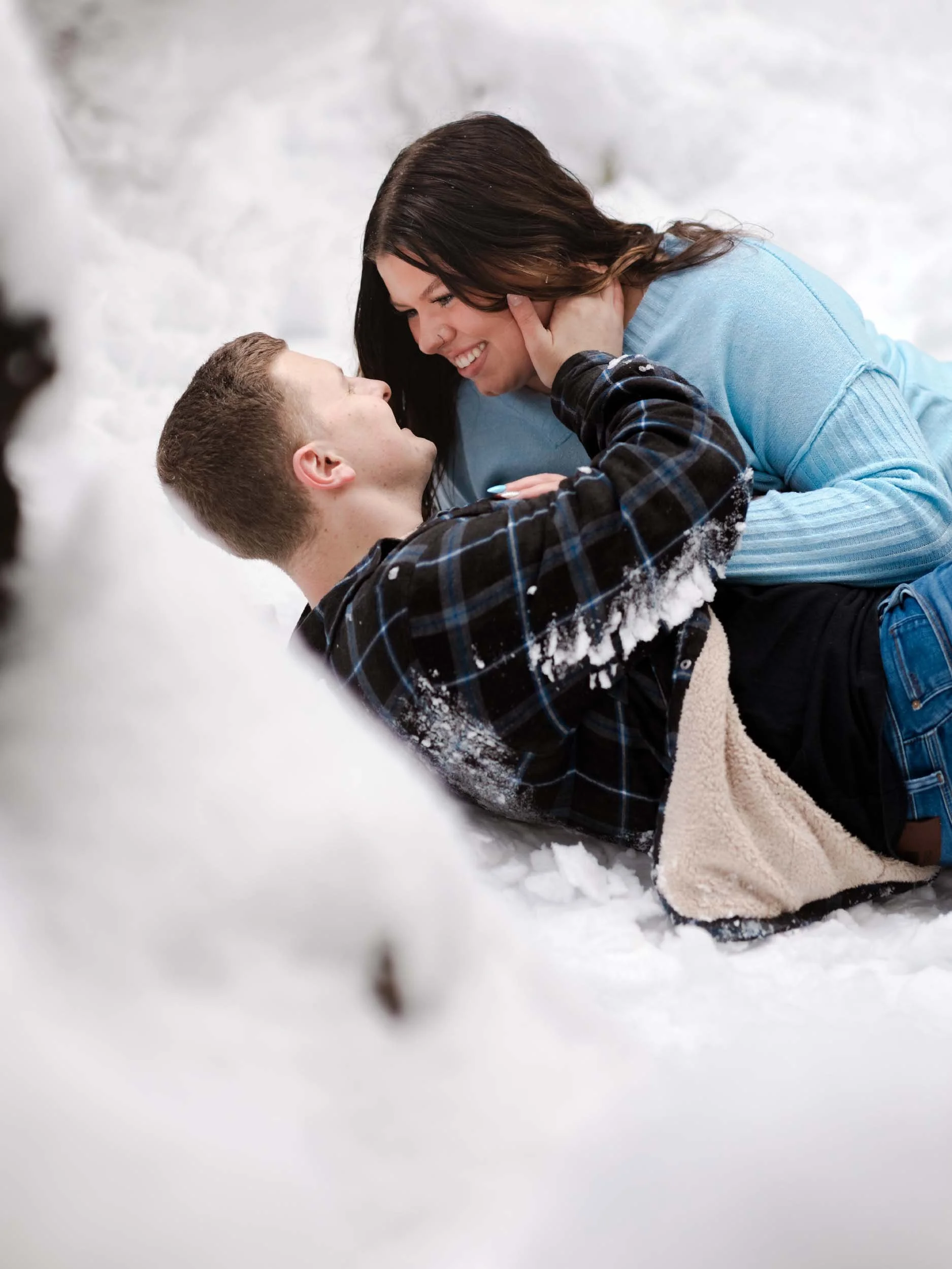 A smiling couple lay in the snow during an engagement session in Mount Baker Snoqualmie National Forest.