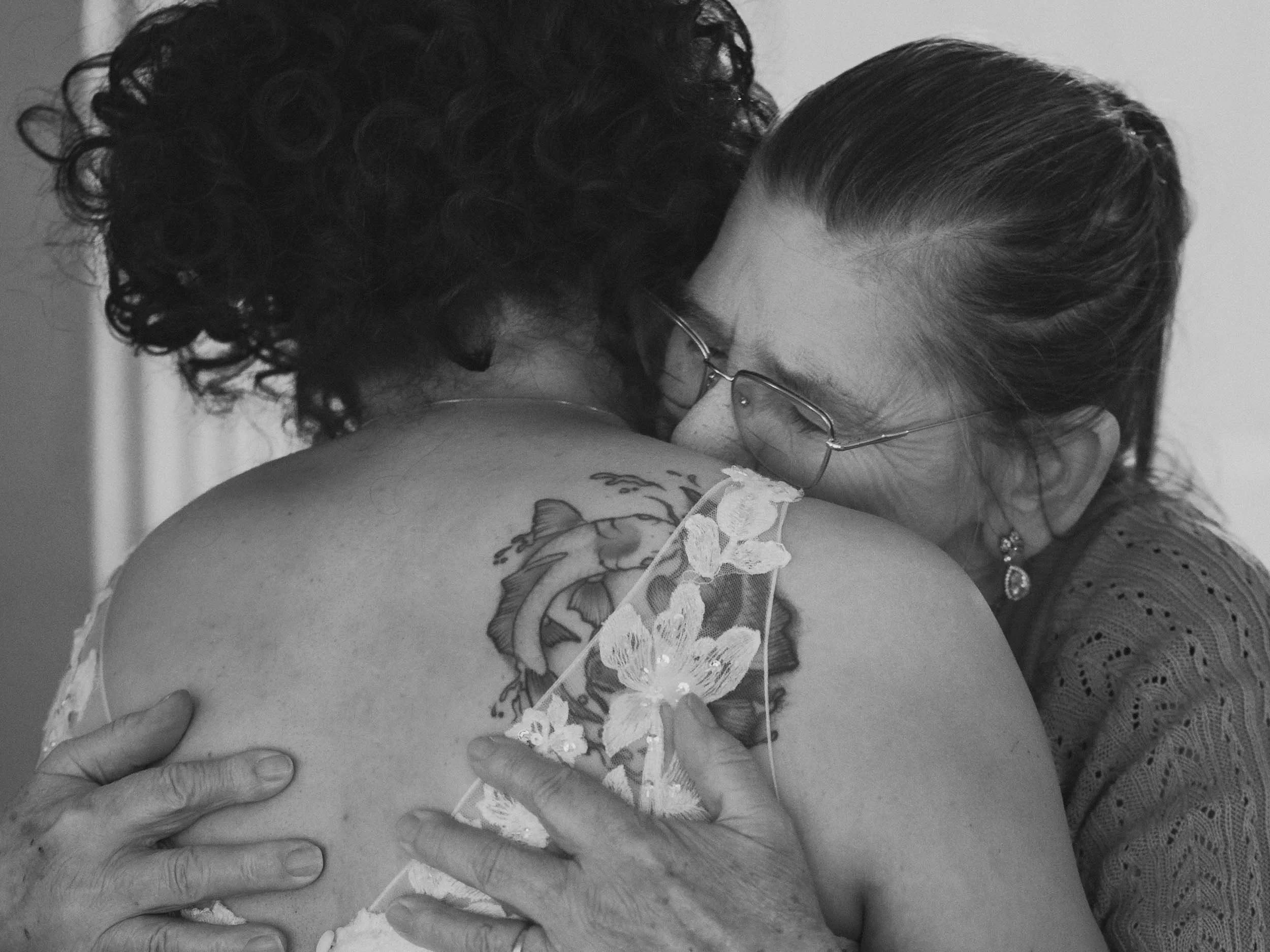 A grandmother hugs the bride with emotion after her dress reveal on her wedding day in Oak Harbor, edited in black and white.