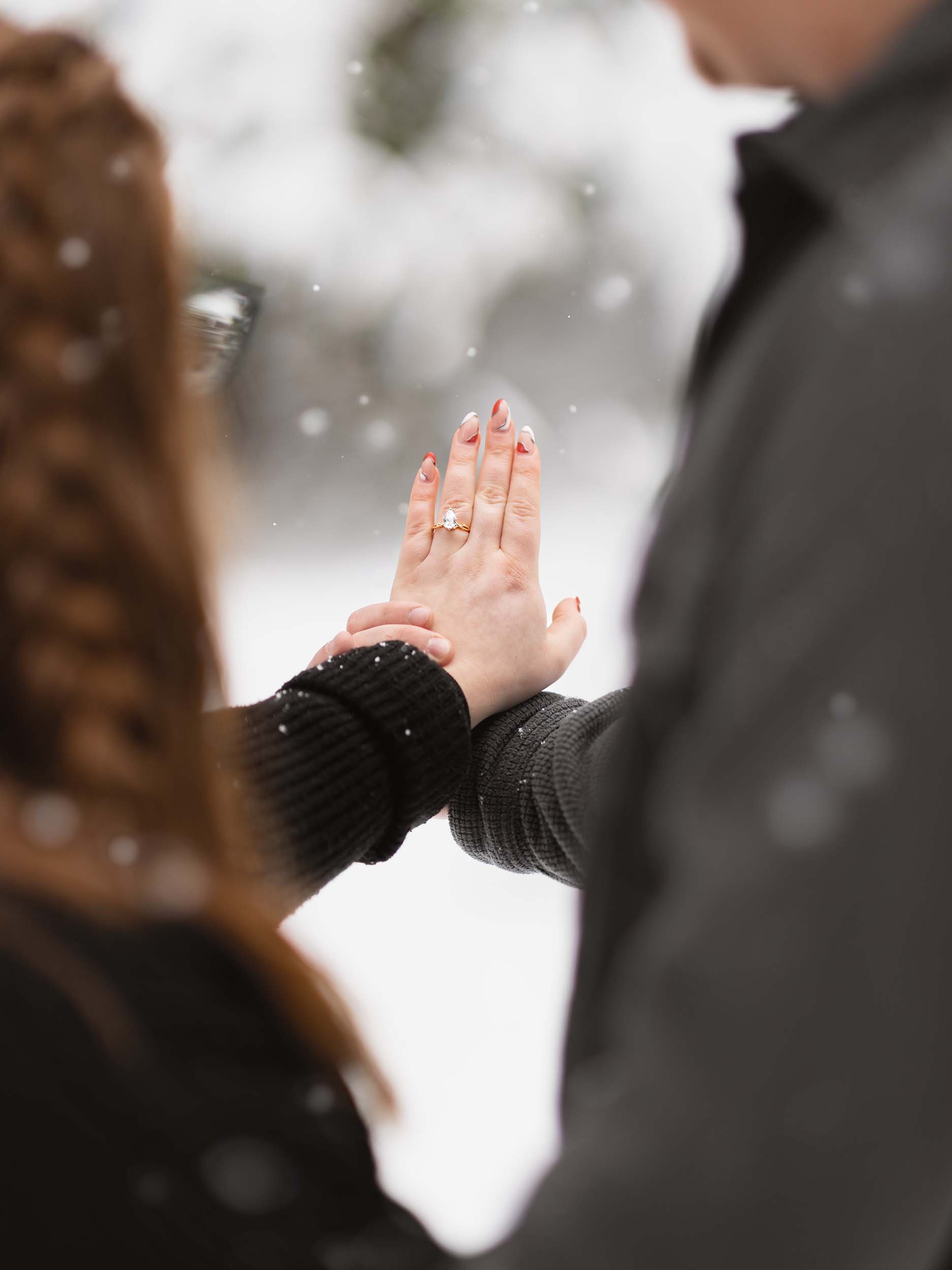 A couple holding hands outdoors in a snowy setting, showing an engagement ring on the woman's finger at their Mount Rainier photography session.