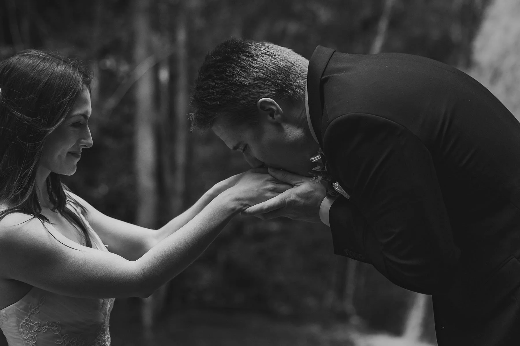 A man in a suit kisses his bride's hands to warm them as she smiles lovingly. Edited in black and white.