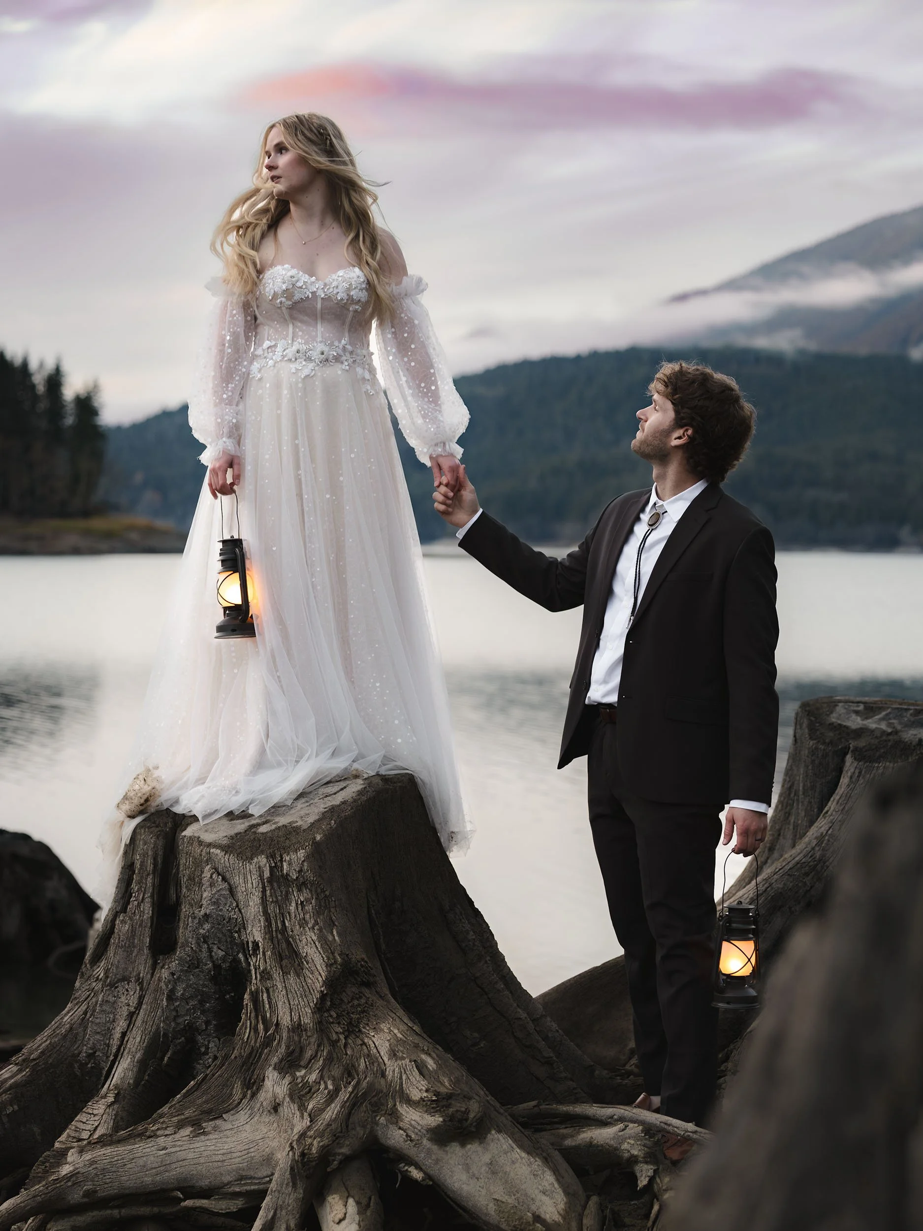Wedding couple hold lanterns at Greider Lake with a pink sunset sky.