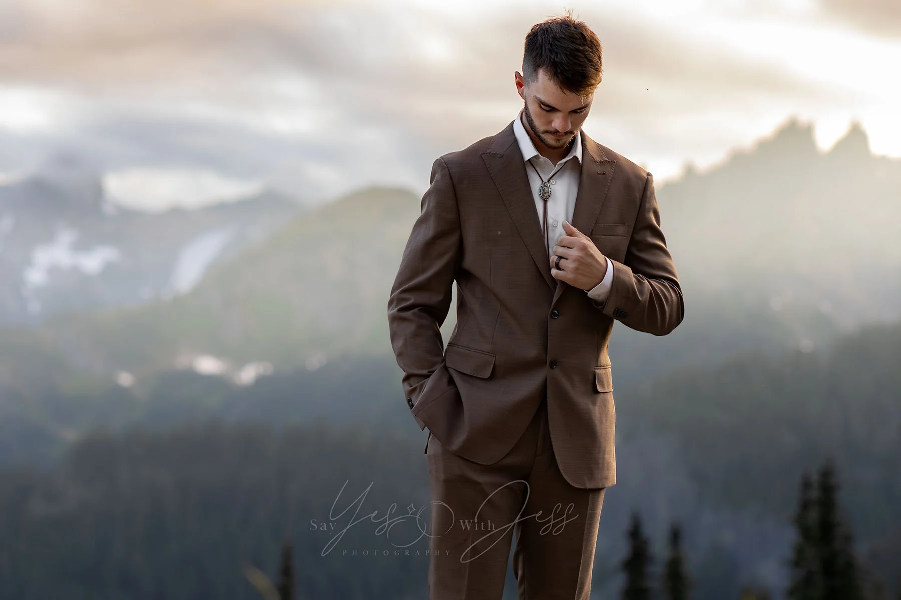 A man in a brown suit poses on his wedding day with a backdrop of the cascade mountain range at sunset.
