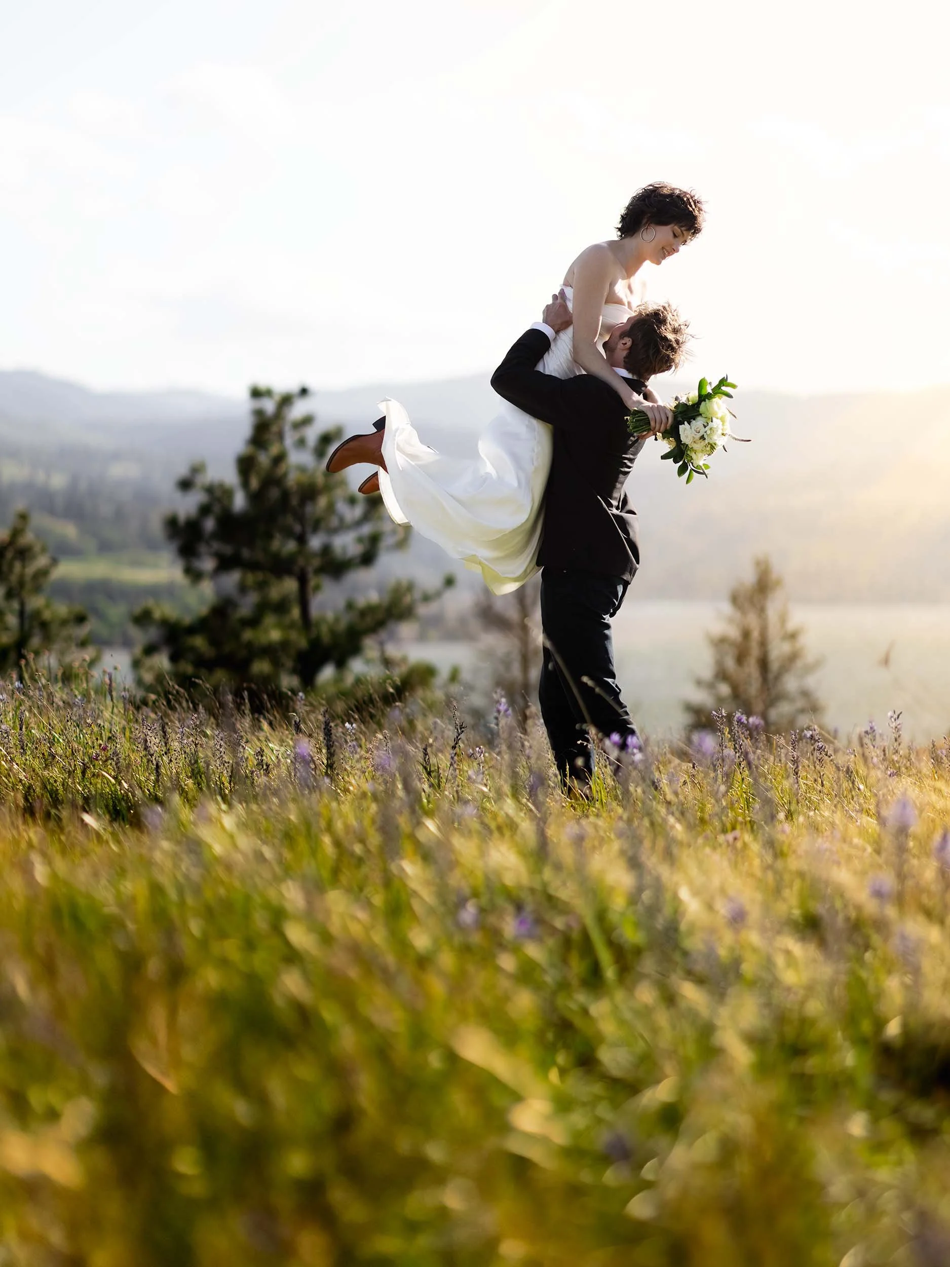 The groom lifts his bride in a meadow overlooking the gorge at sunset at their Washington micro wedding.