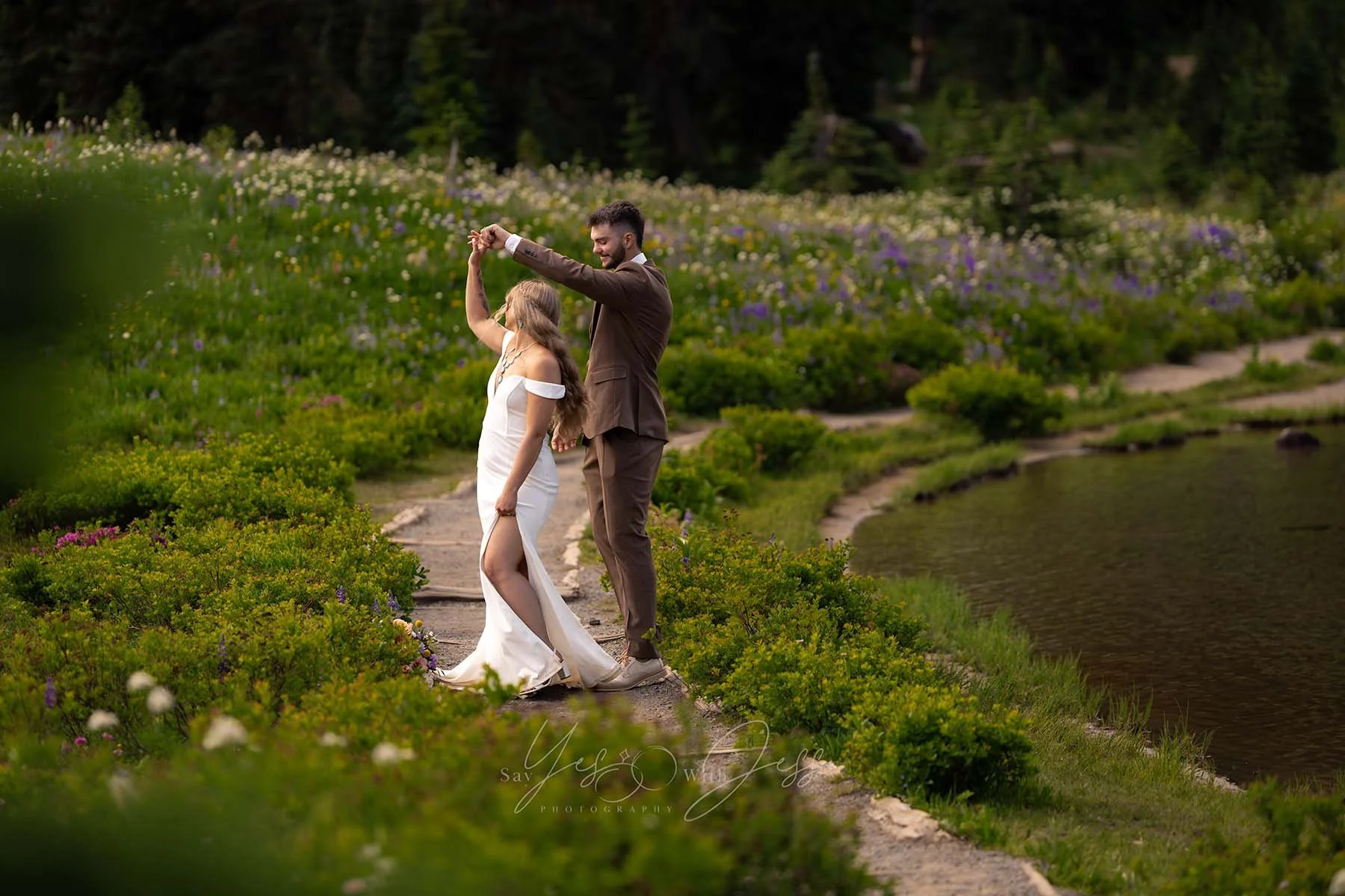 A man twirls his bride, dancing on a path around Tipsoo Lake, surrounded by vibrant subalpine wildflowers on their elopement day.