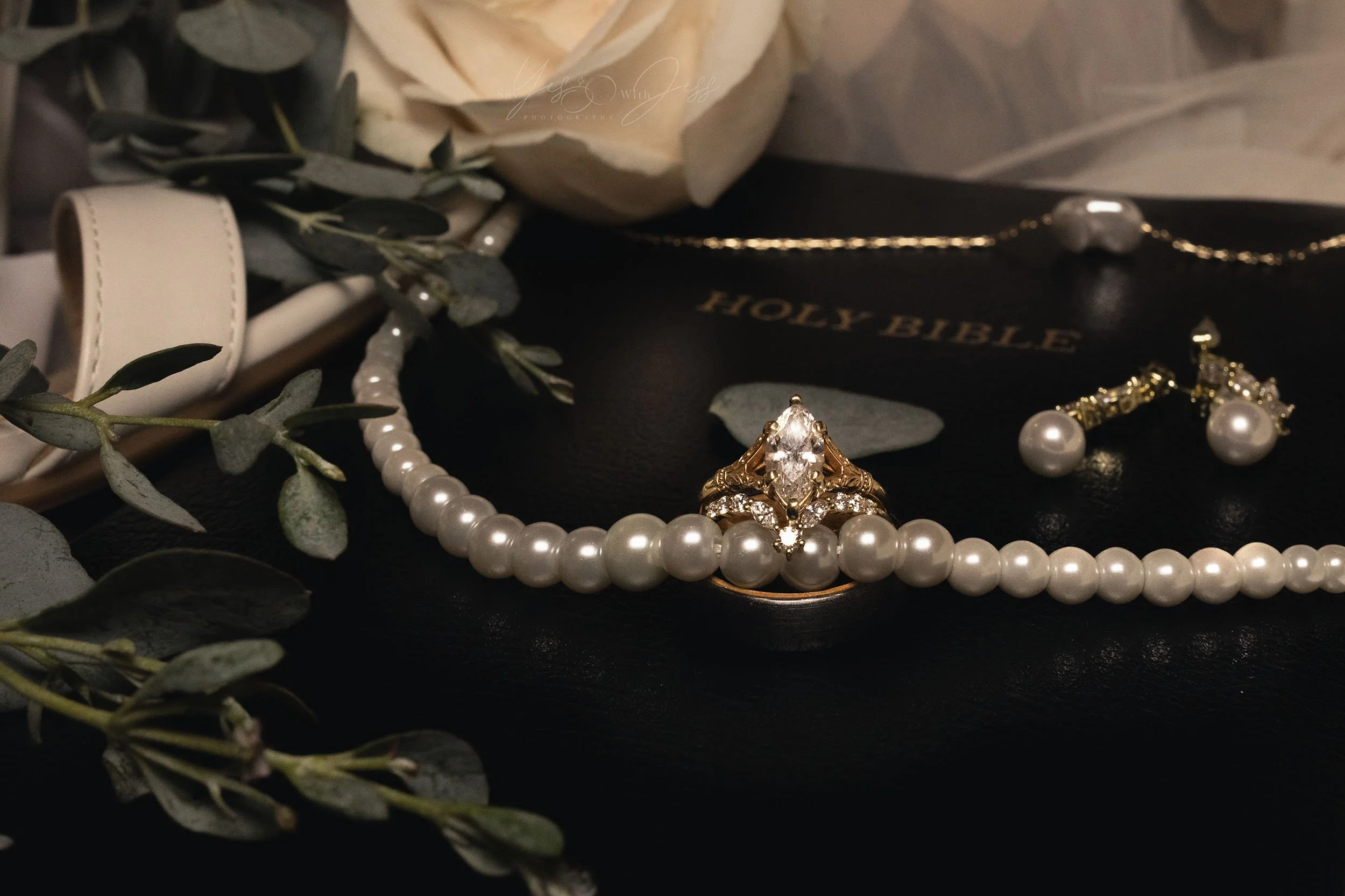 A wedding flat lay centered on rings in a green ring box and framed by the invitation suite. 