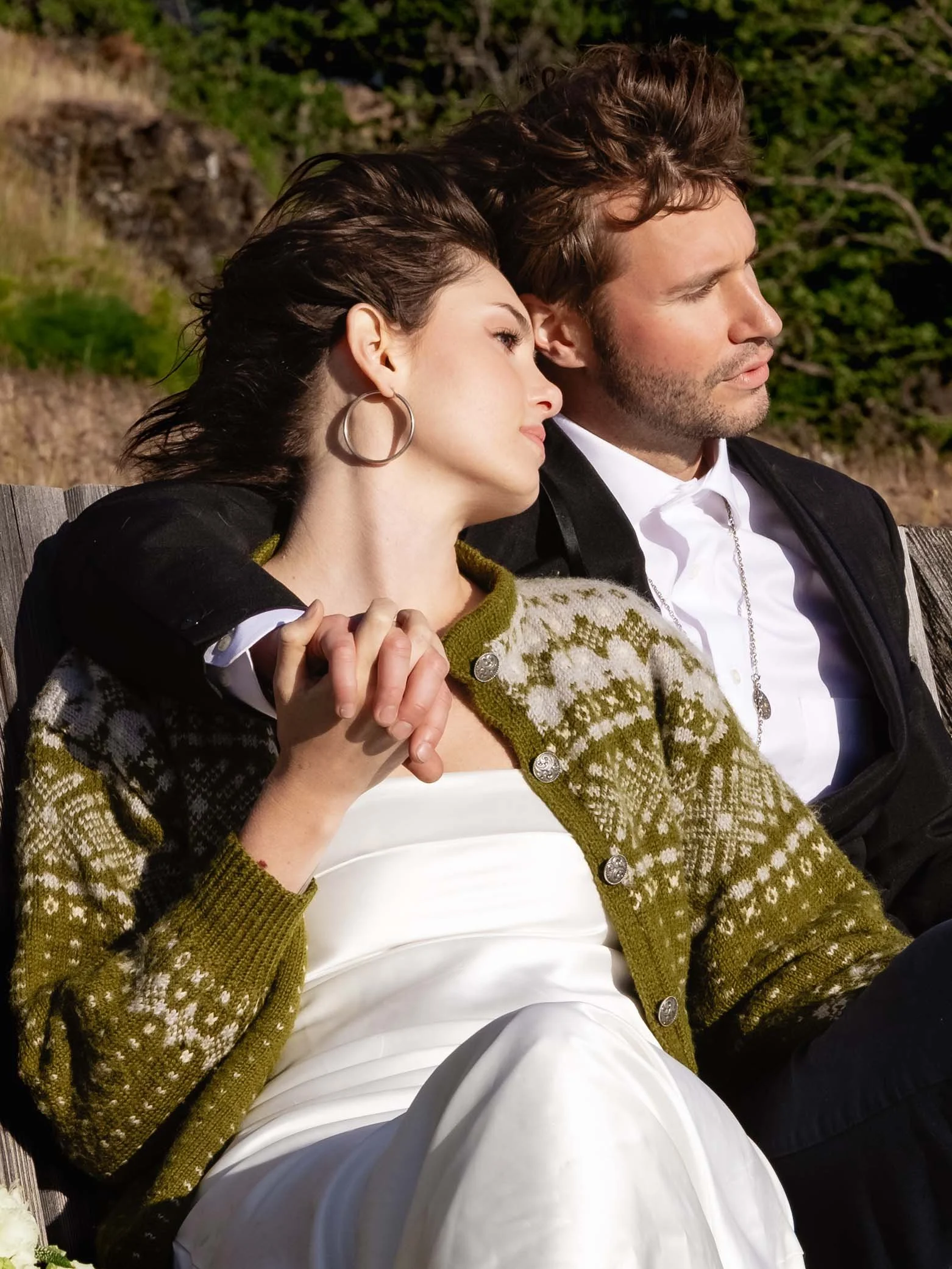 Editorial wedding couple sit on a bench holding hands, watching the sun set on the Columbia River Gorge.
