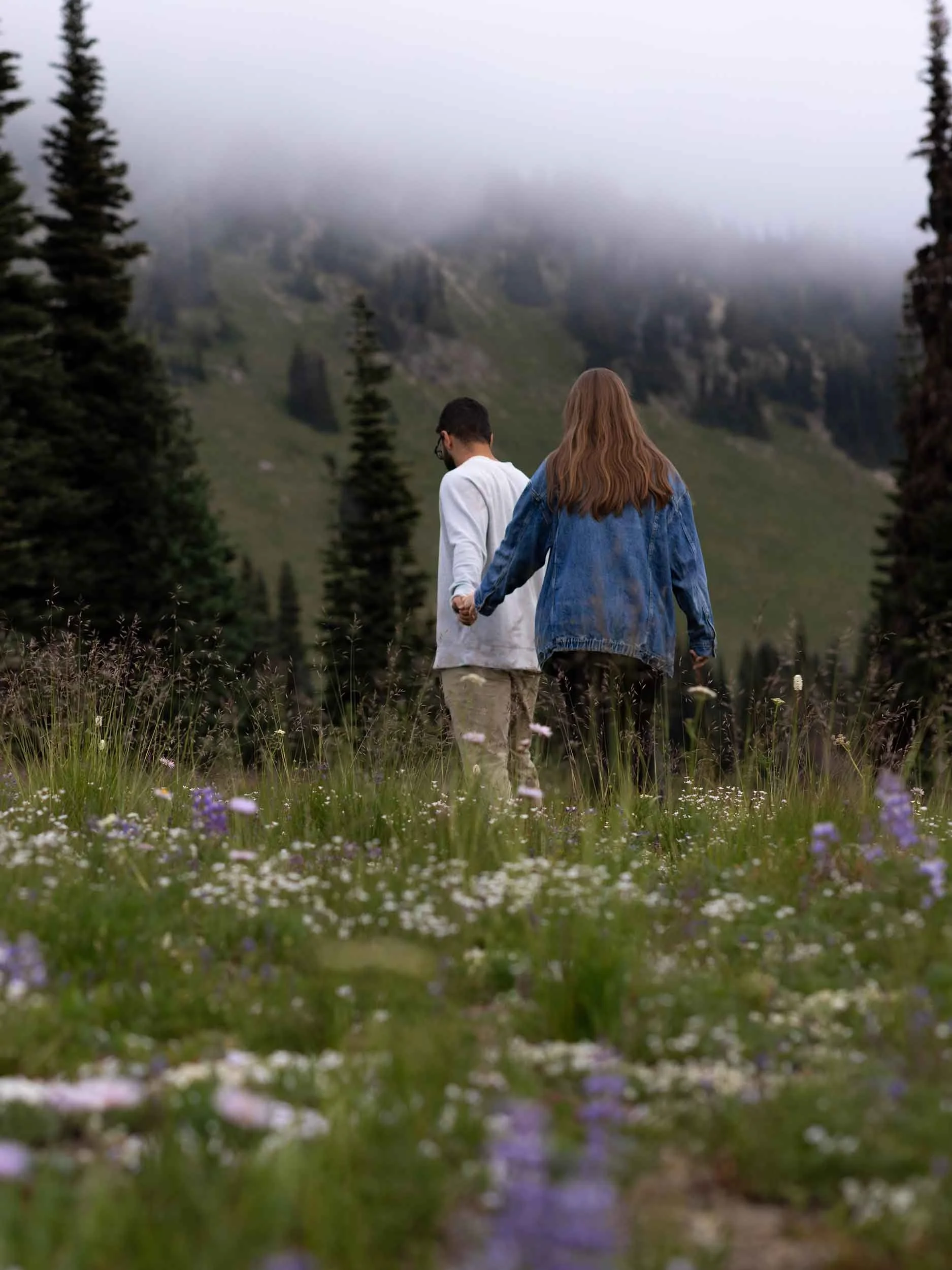 James leads Kasey through a field of wildflowers and moody PNW fog at Mount Rainier after he proposes.