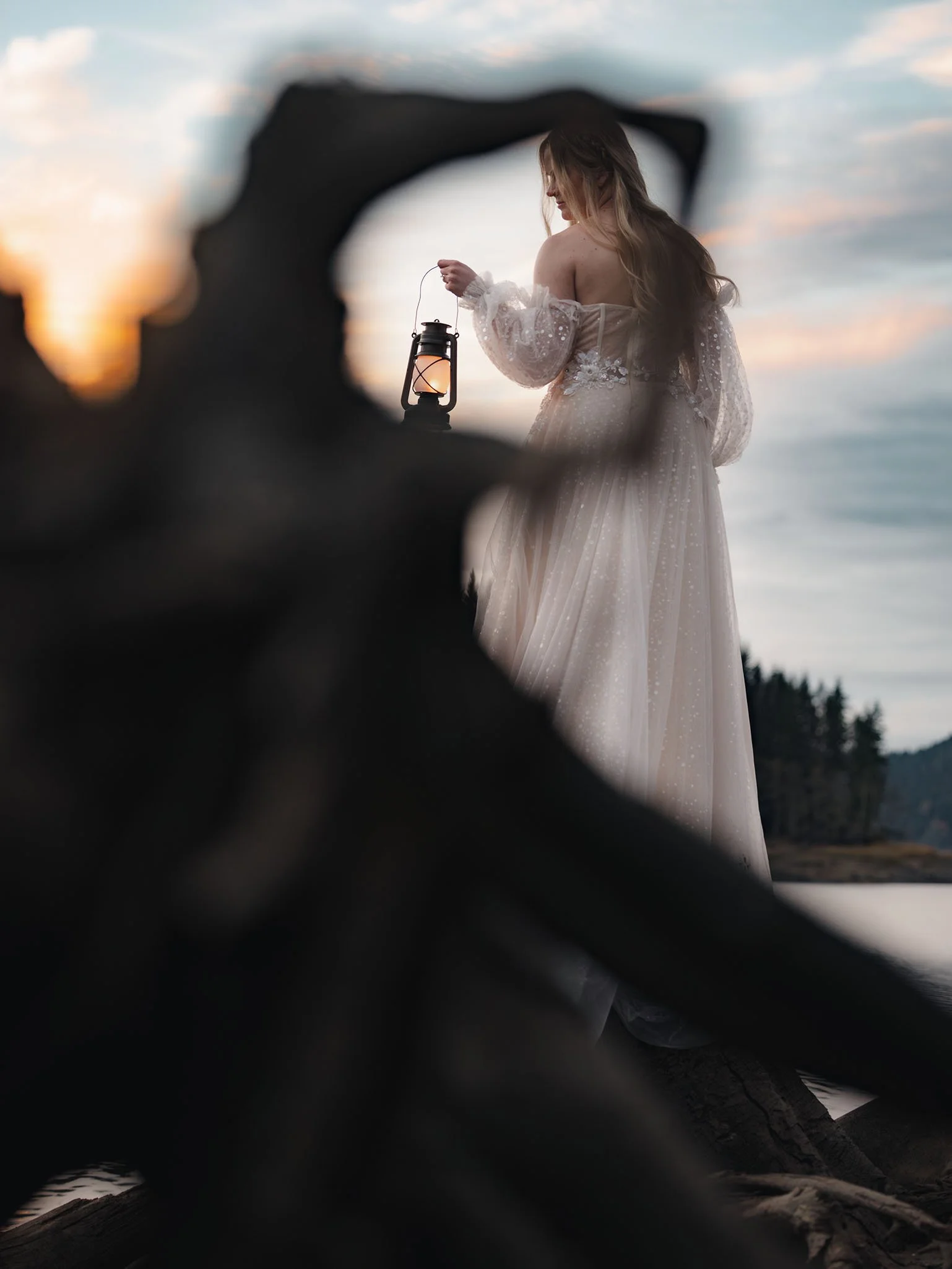 Artistic perspective of a bride holding a lantern at sunset through old growth tree roots during a Sultan, Washington elopement.