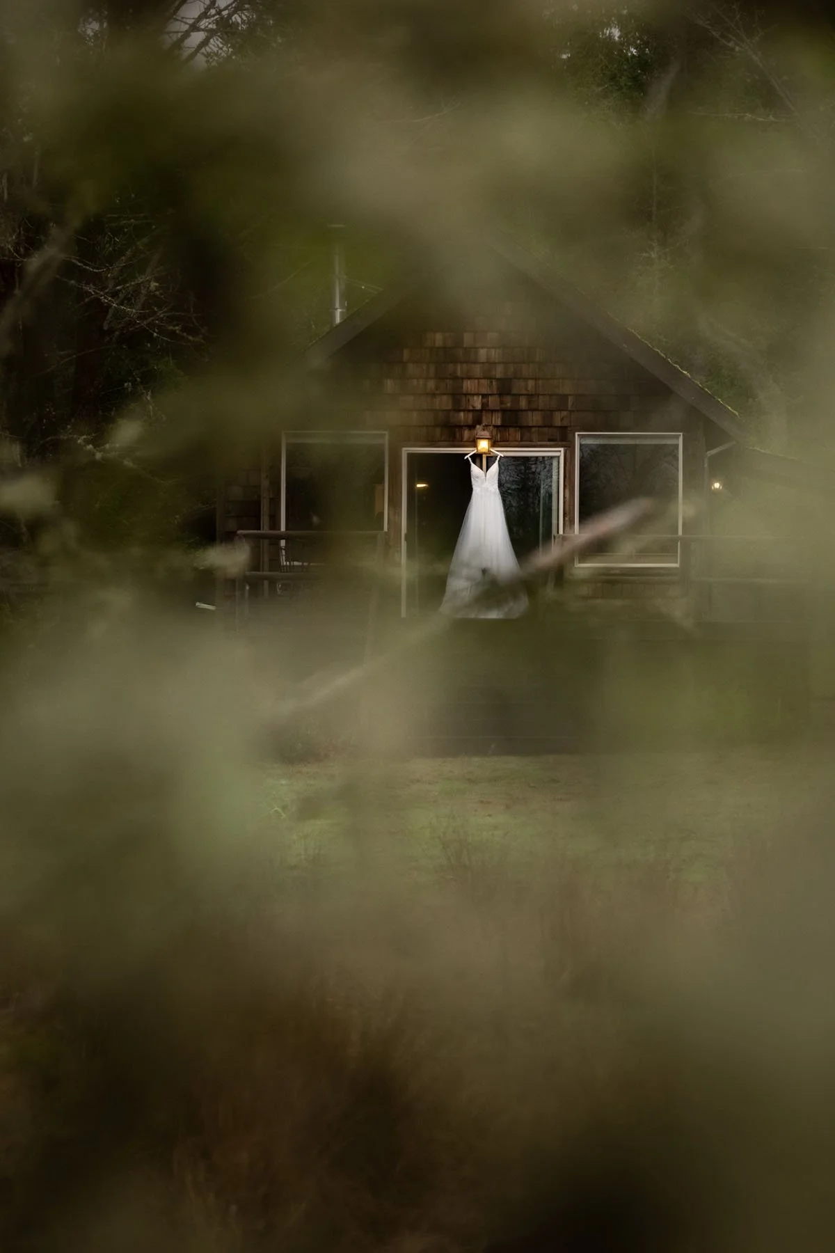 Perspective through a tree with focus on a wedding dress hanging on a cabin porch light in Port Angeles