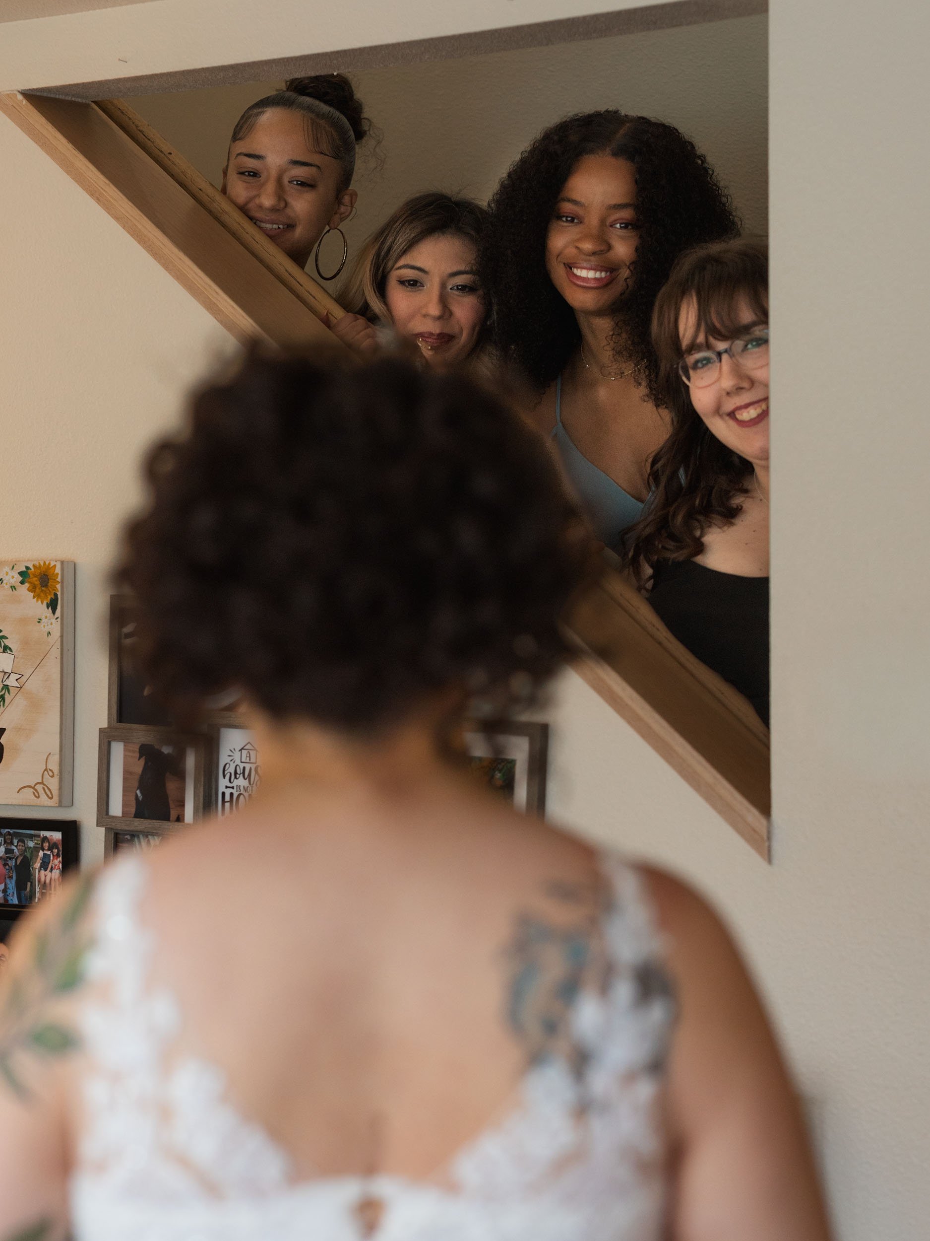 Bridesmaids smile through the cutout on the stairs during the bride's dress reveal before her Oak Harbor wedding.