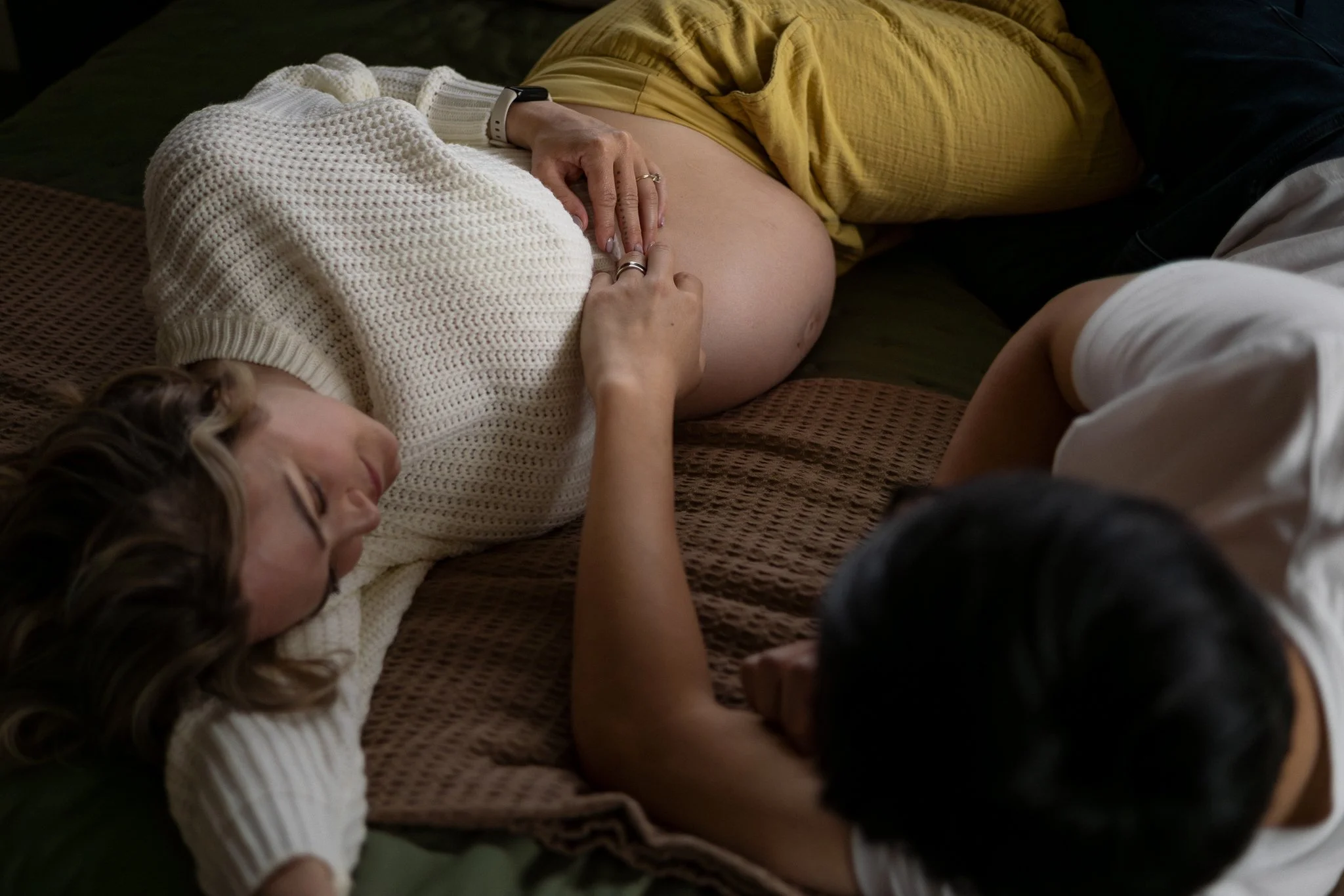 Lifestyle maternity couple lay in their bed, resting their hands on her pregnant belly in Bonney Lake, Washington.