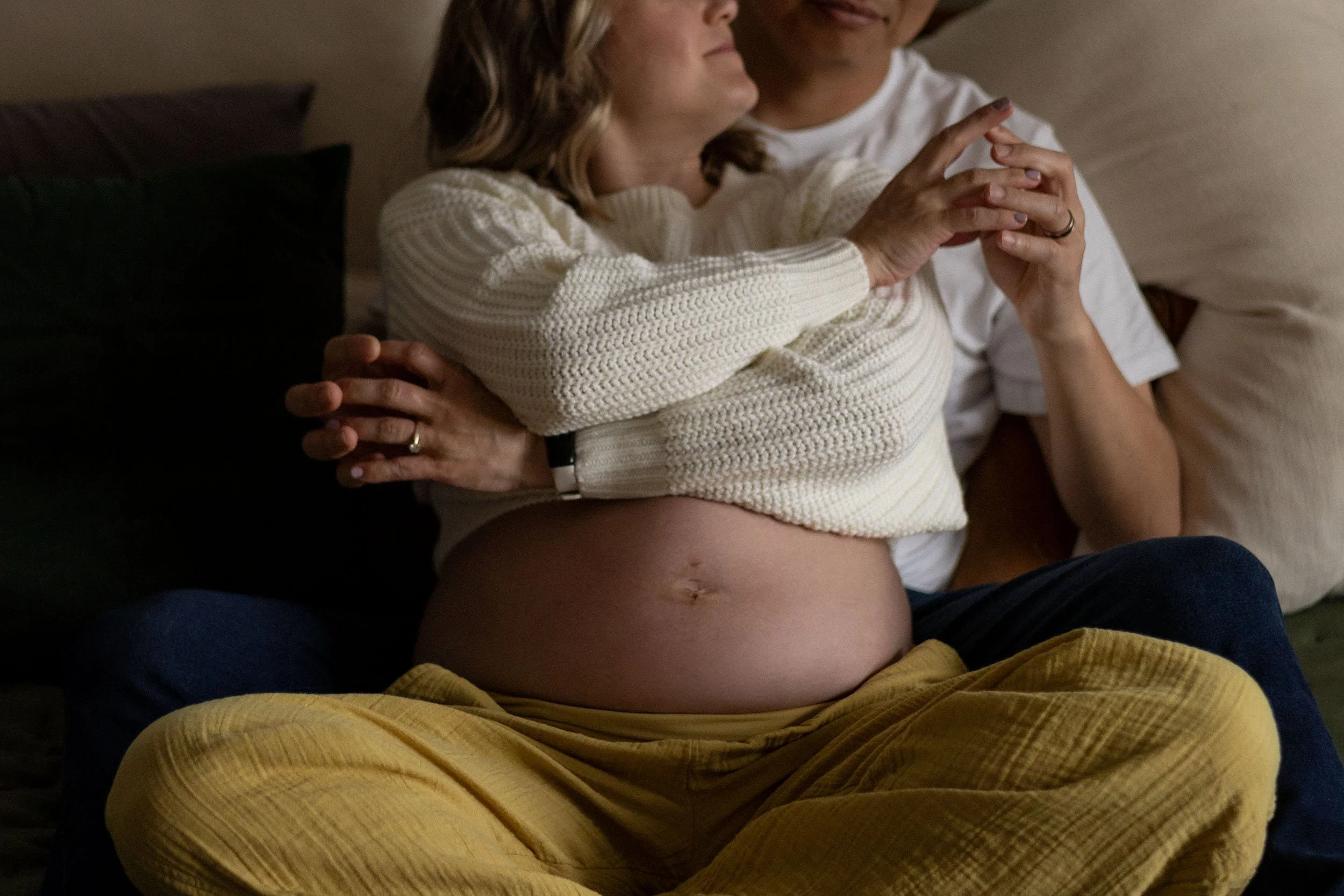 Lifestyle maternity couple sit in bed, delicately intertwining fingers during a session in Bonney Lake, Washington.