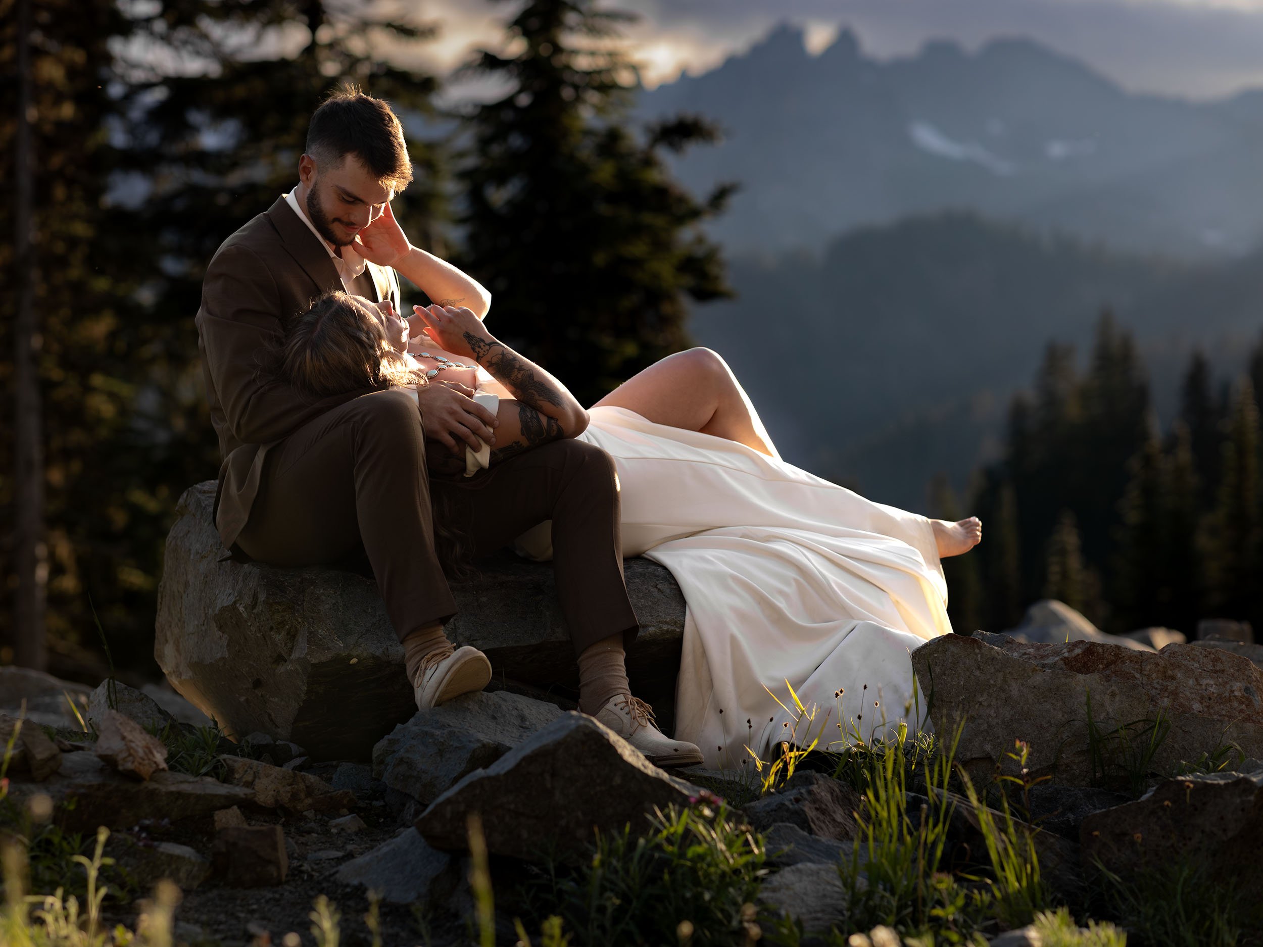 Bride lays in her husband's lap on a large rock with sprawling views of the Northern Cascades at their Mount Rainier sunset elopement.