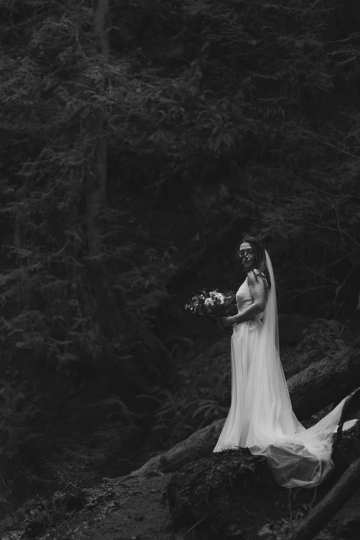 Dramatic black and white edit of a woman in a wedding dress holding a bouquet with her hair blowing in the wind.