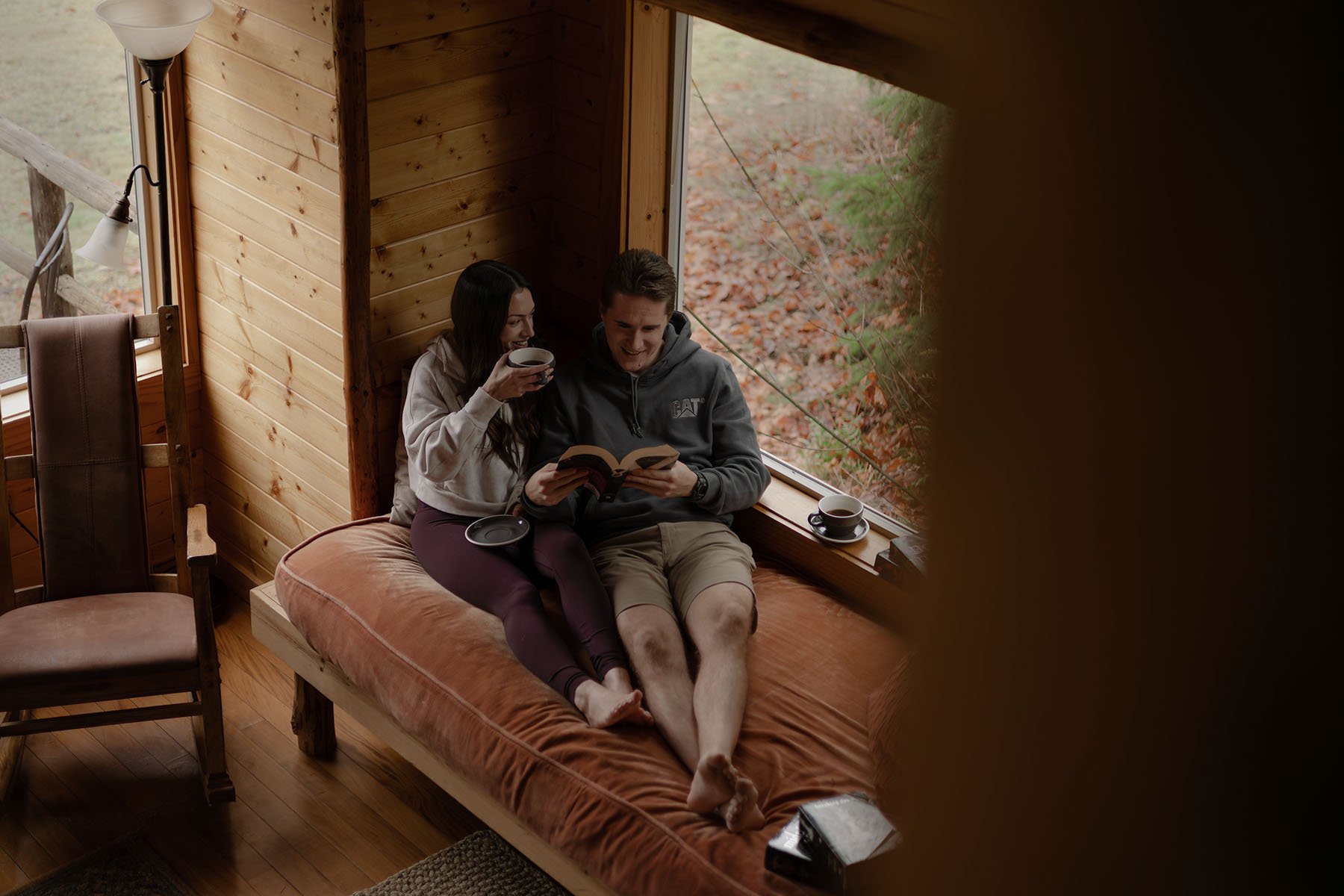 A couple lounge on a cabin daybed drinking coffee and reading before their Olympic National Park elopement.