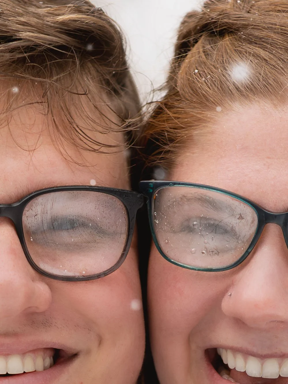 Close-up of an engaged couple with similar features, their faces close together, both smiling with glasses fogged up from the cold, snowy environment during their engagement session near Mount Rainier.