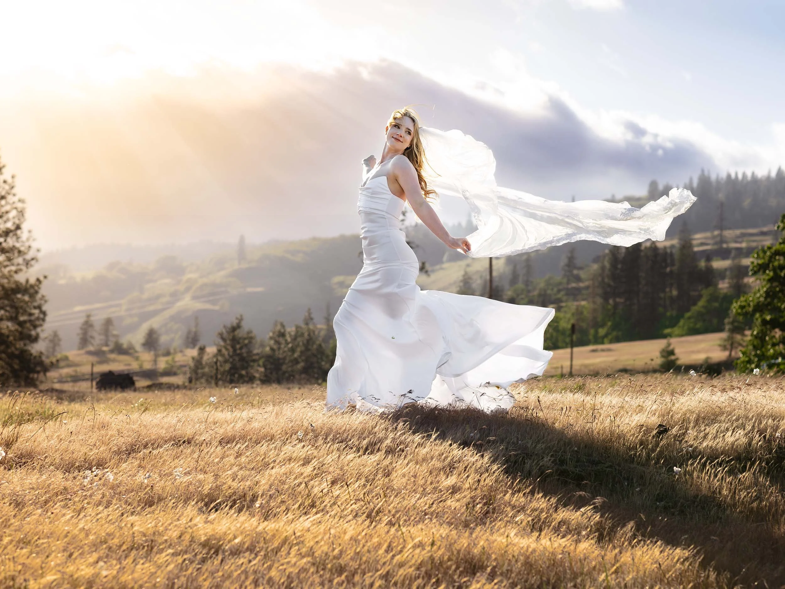 Editorial bride walks through a meadow at sunset as the wind blows her veil and dress wildly at a Columbia River Gorge bridal session.