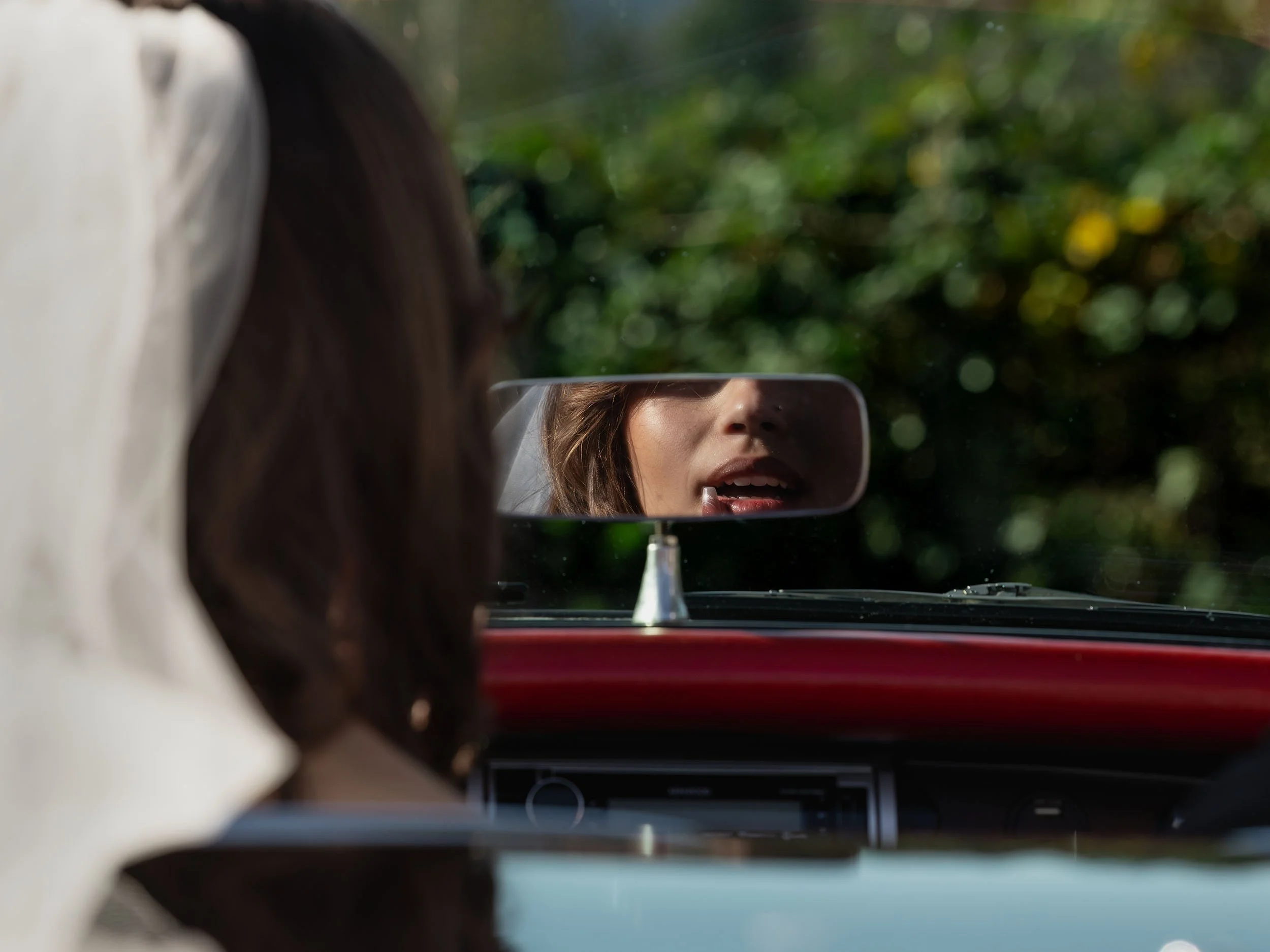 Perspective of editorial bride fixing her lipstick in rearview mirror of a vintage corvette convertible near Seattle