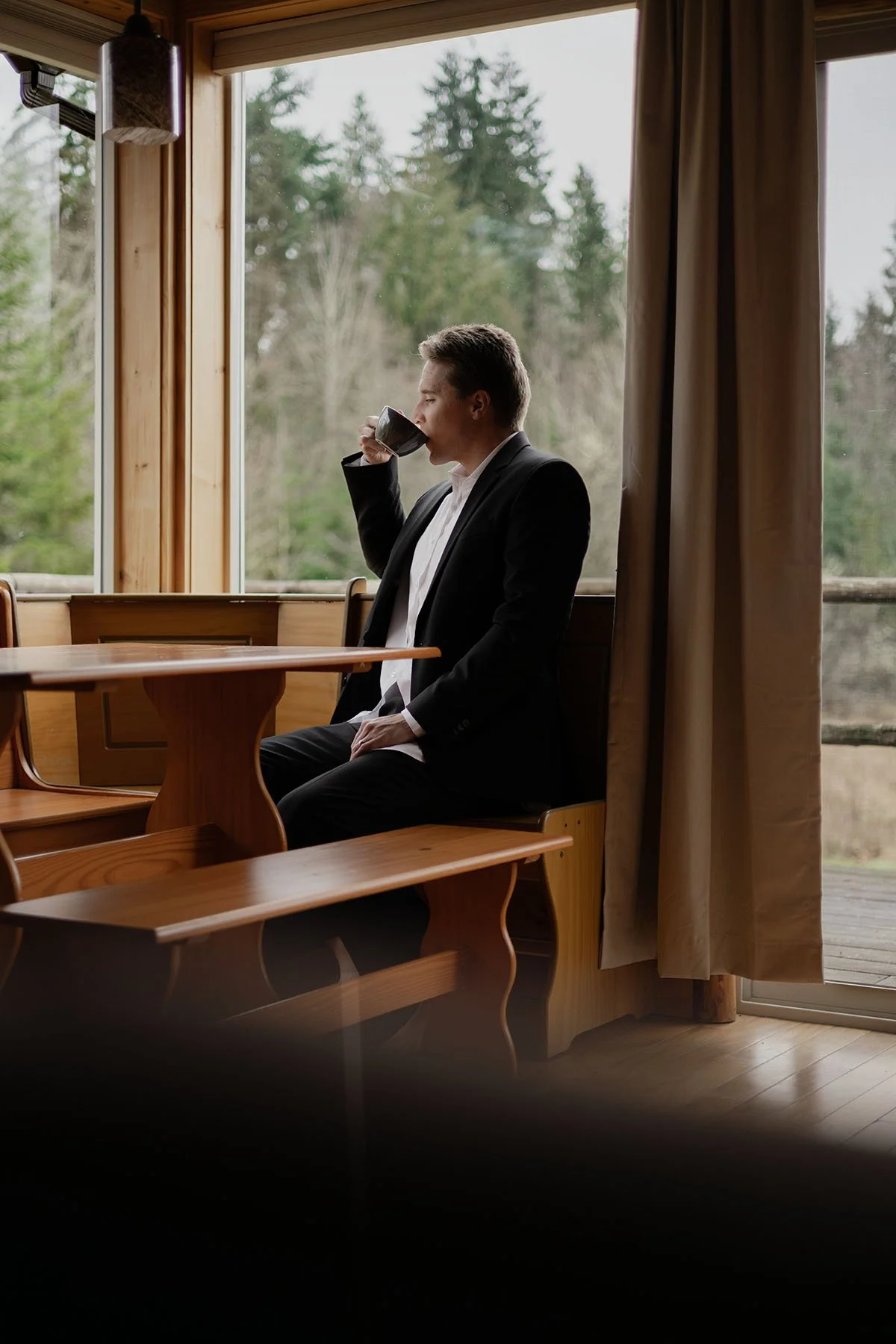 A man in a suit drinks coffee sitting in a Port Angeles cabin on his wedding day