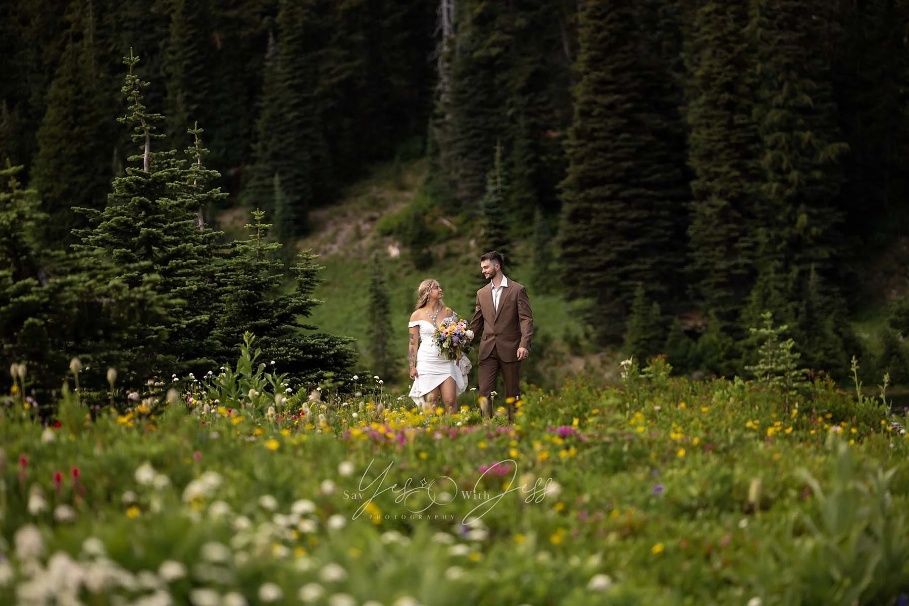 A couple in wedding attire stand in a meadow of subalpine wildflowers on their wedding day at Mount Rainier National Park.